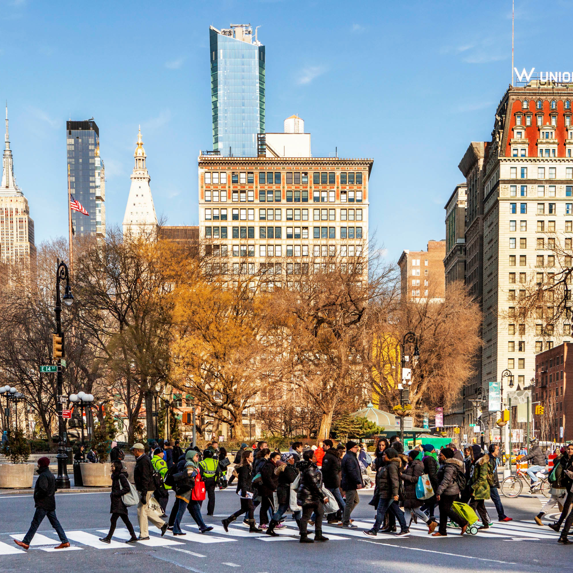 Busy Union Square crosswalk in New York City with pedestrians and skyline views including the Empire State Building