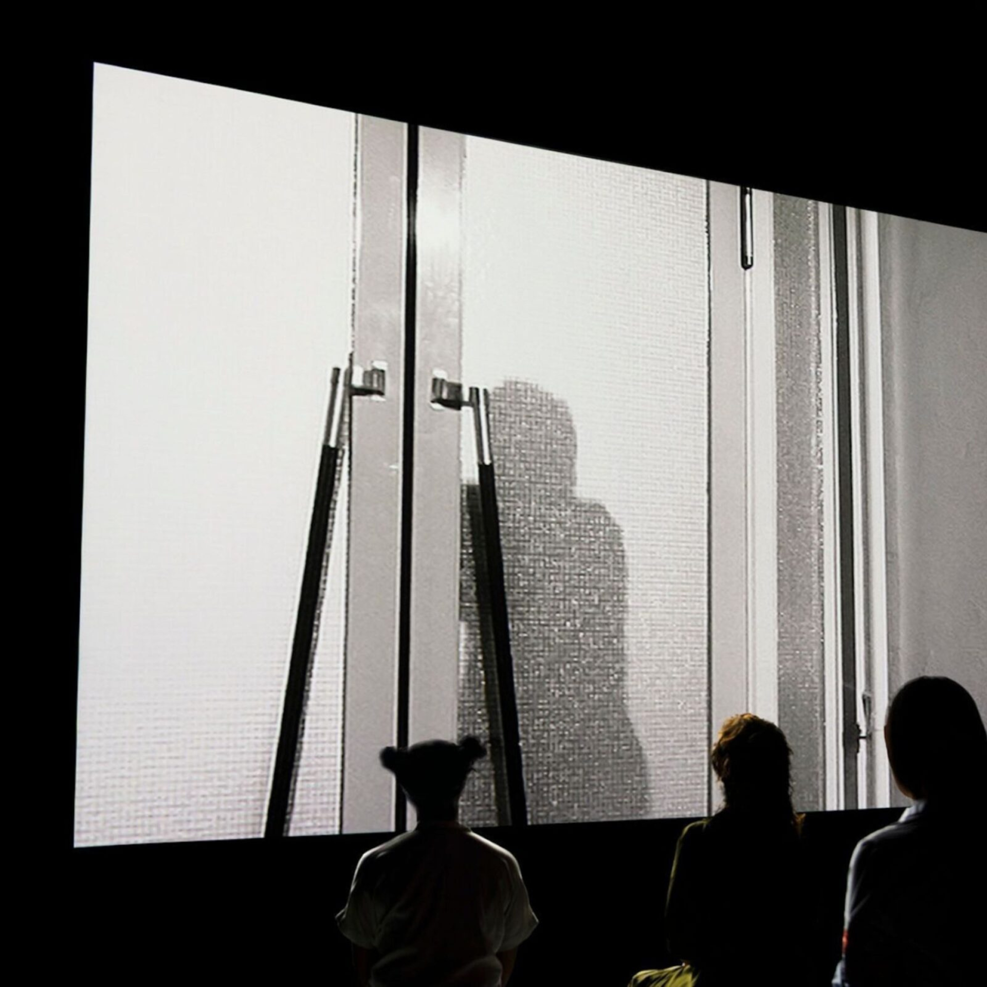 Best Museum Exhibits in NYC Spring 2026: Silhouetted audience watching a black‑and‑white film scene of a figure behind a glass door