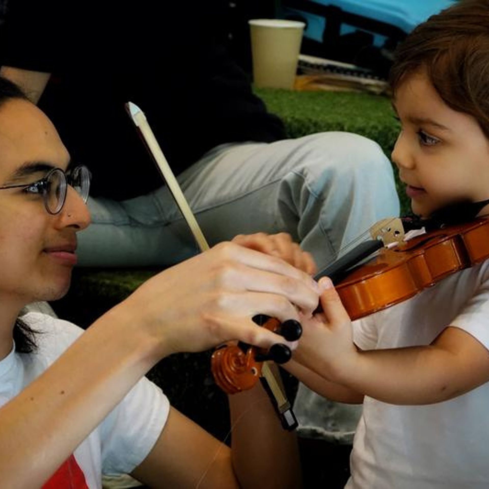 Adult guides child during a violin lesson, showing how to hold and play the instrument