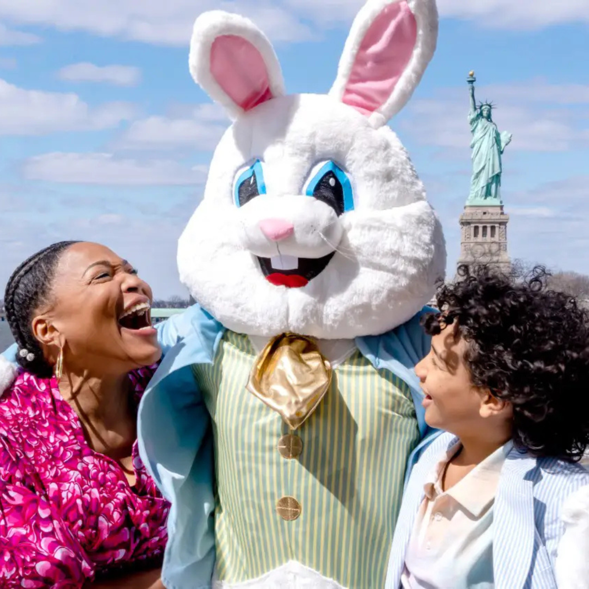 Person in Easter Bunny costume posing with a smiling woman and child near the Statue of Liberty