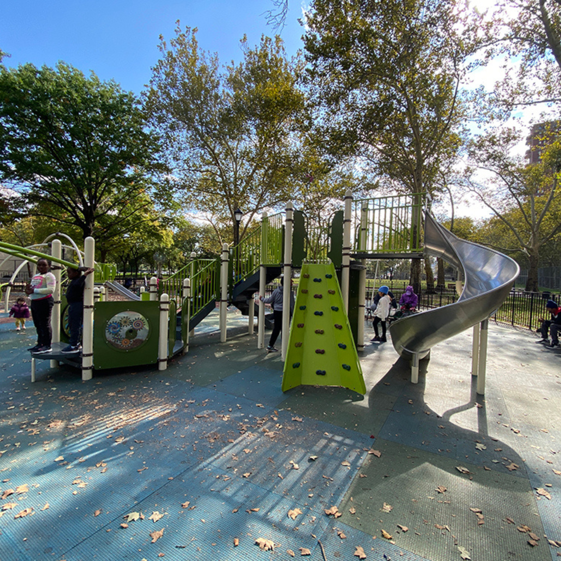 Children and adults enjoying a sunny autumn day at a playground with climbing wall, slide, and play structures