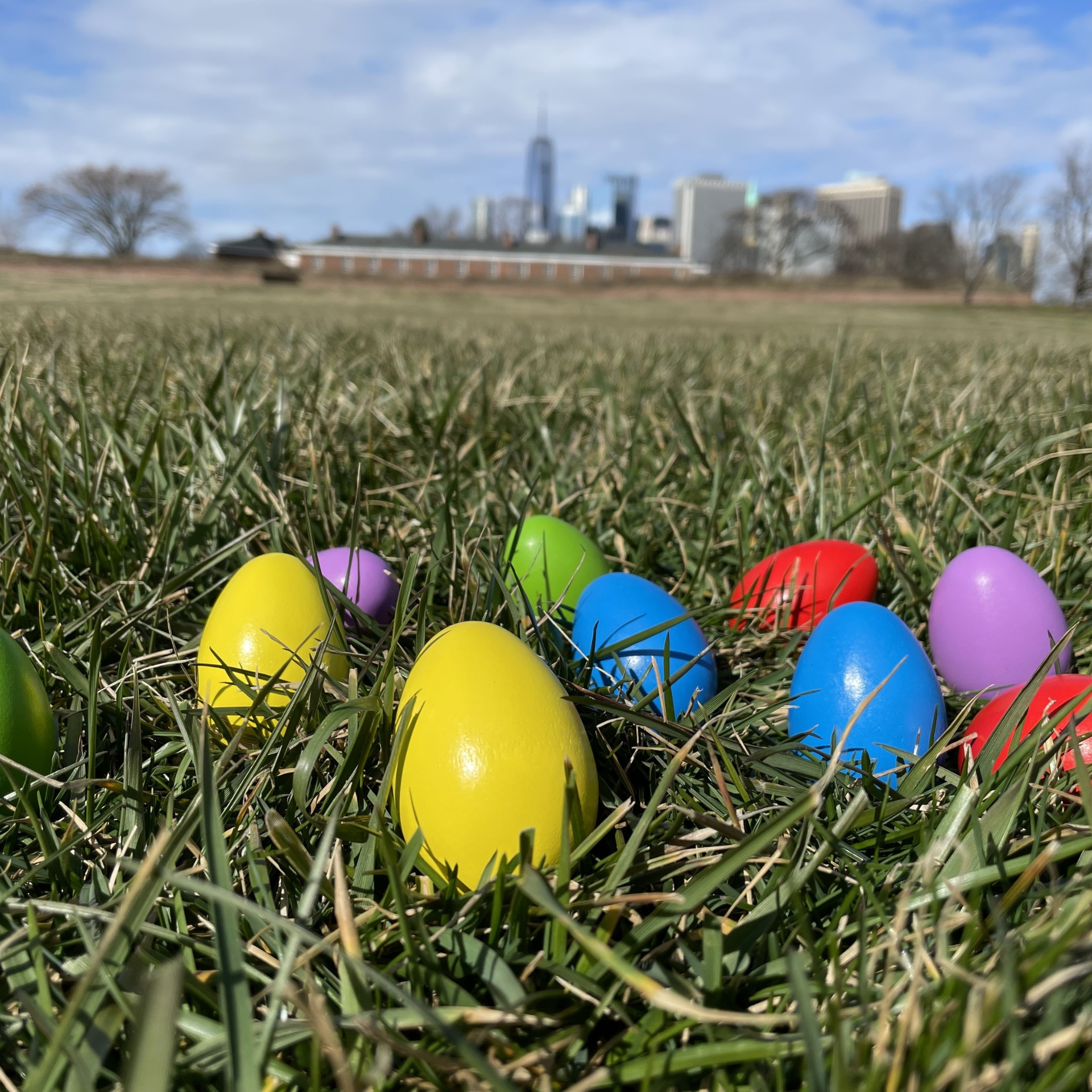 Colorful plastic Easter eggs scattered on grass with a city skyline in the background