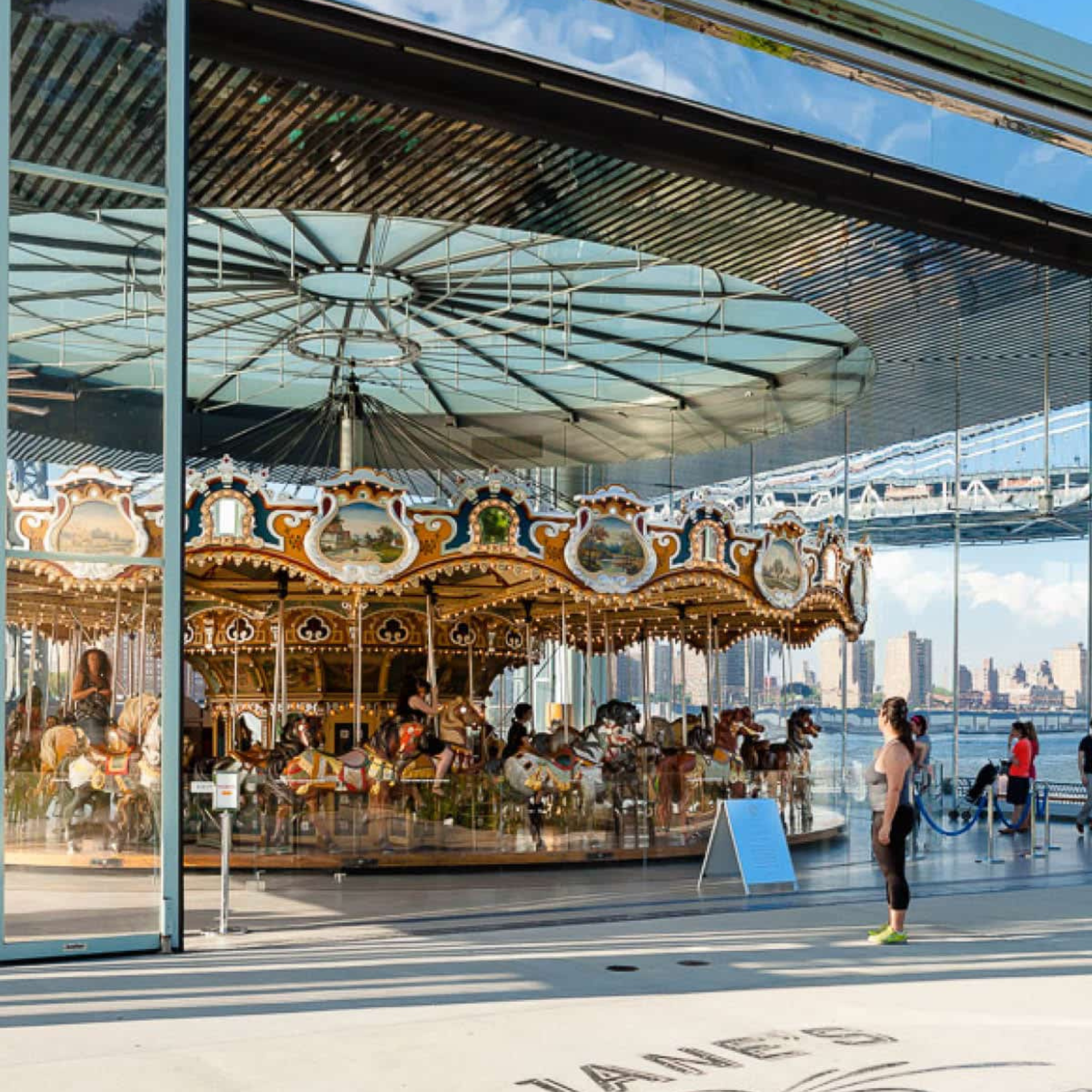Vintage carousel with ornate horses inside a glass pavilion near the waterfront and city skyline