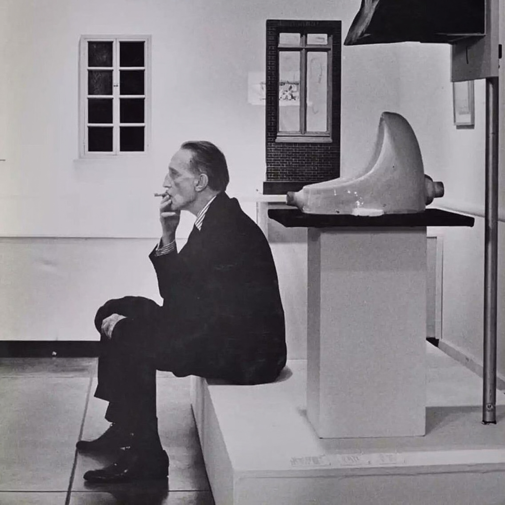 Black-and-white photo of man in suit smoking beside Duchamp’s “Fountain” artwork in gallery