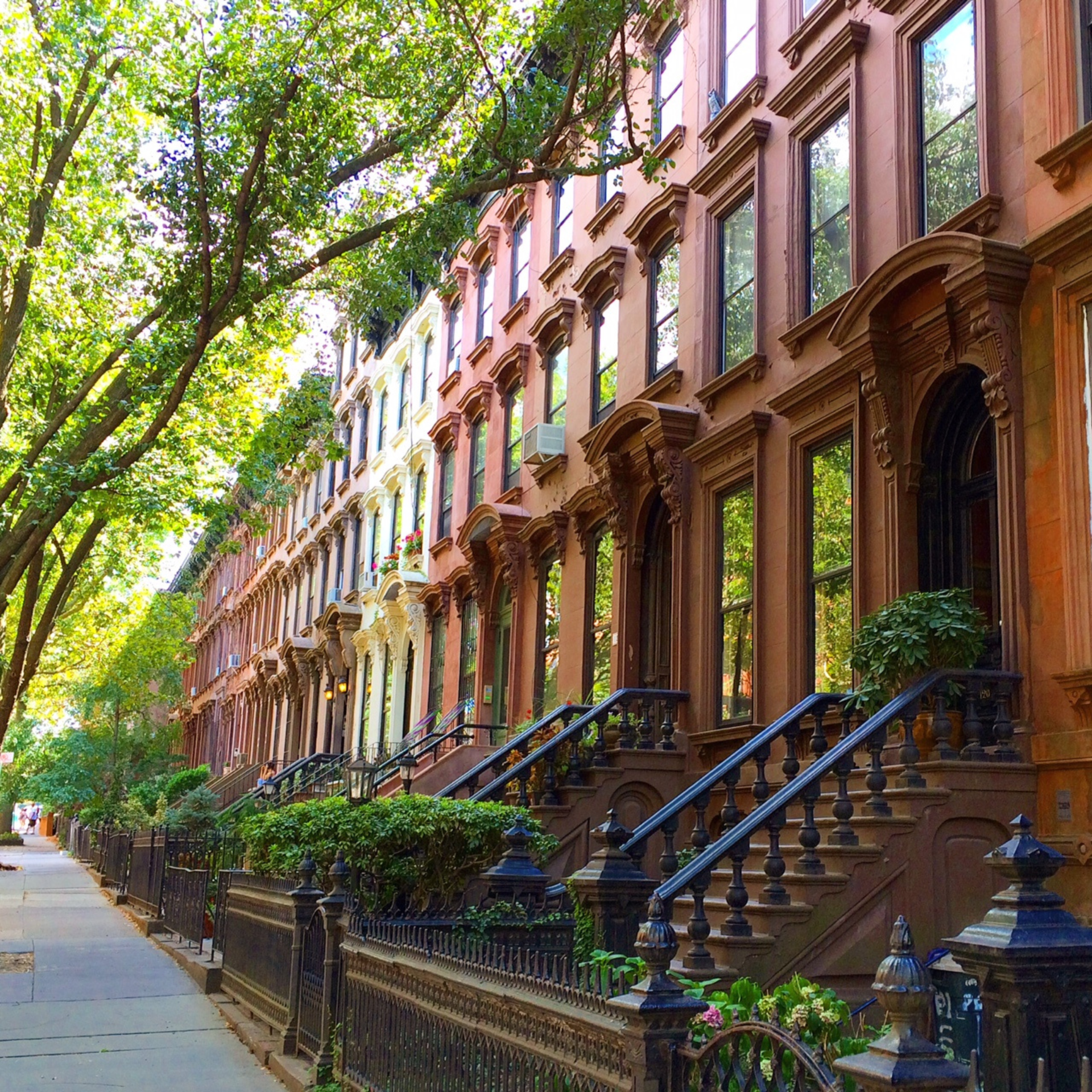 Row of brownstone townhouses with stoops and ornate details along a tree-lined street