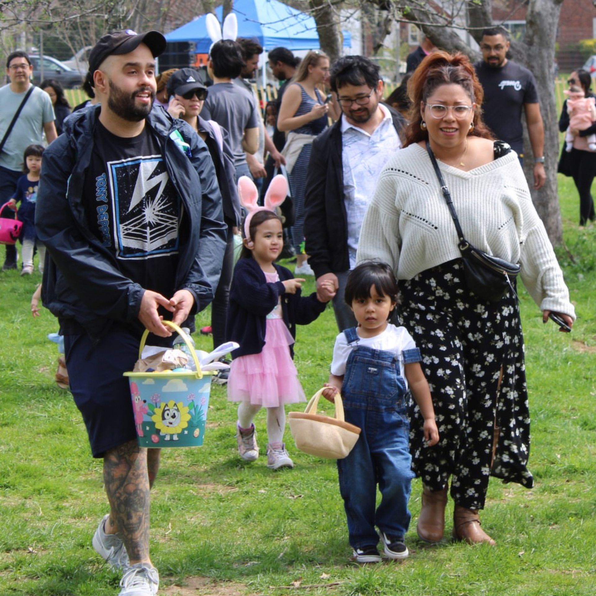 Children with baskets join adults in a lively Easter egg hunt at a park festival