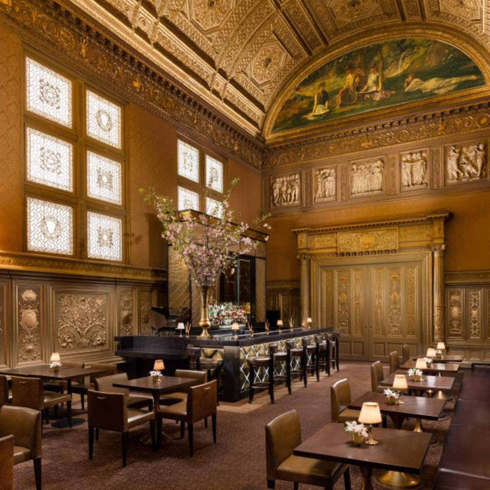 Luxurious restaurant interior with ornate gold ceiling, mural, and elegant bar area with floral centerpiece