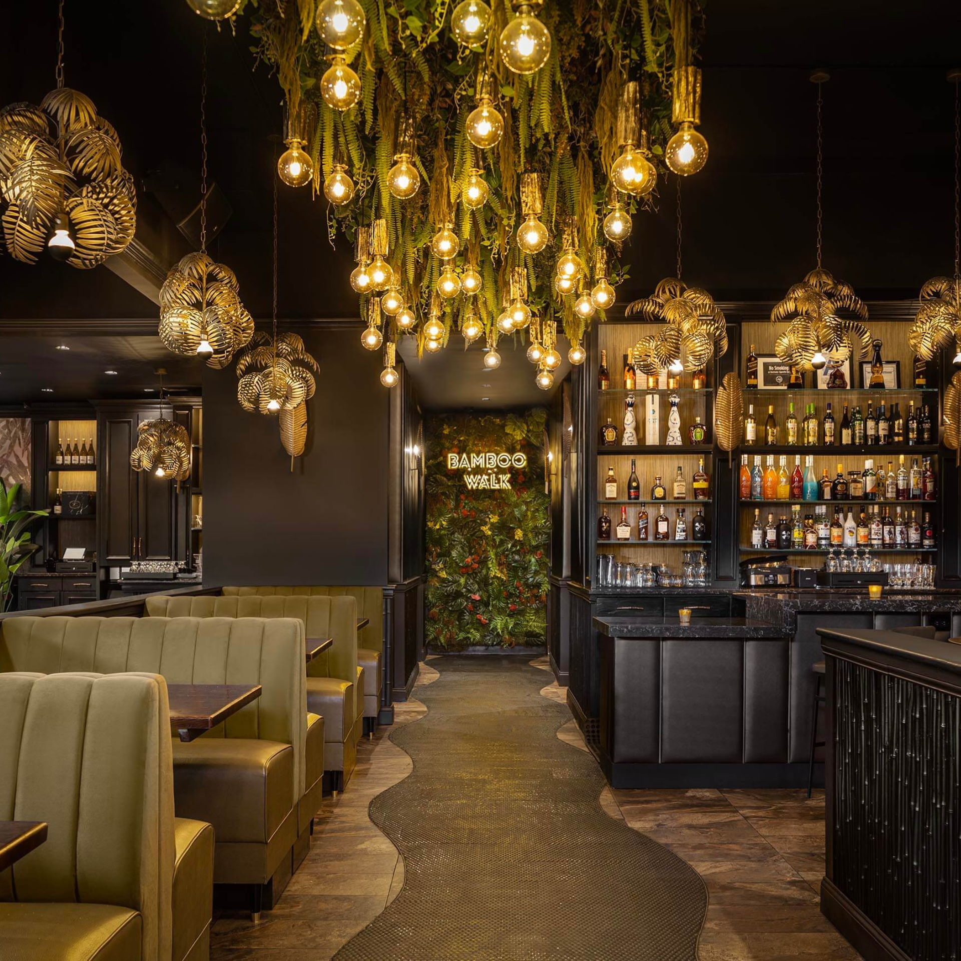 Stylish restaurant interior with green booth seating, tropical-themed lighting, and illuminated “BAMBOO WALK” sign