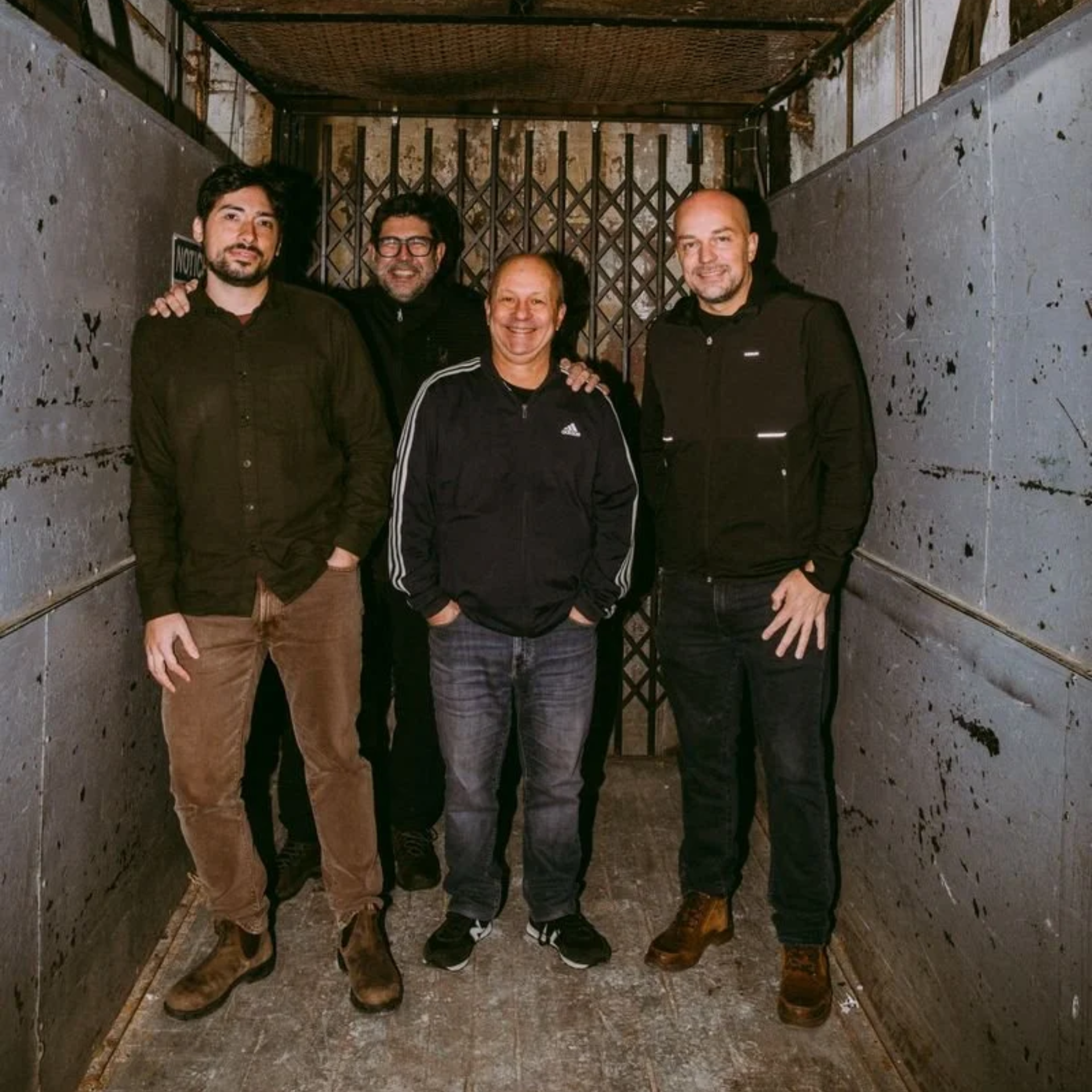 Four people in casual clothing standing inside an old industrial elevator with worn metal walls