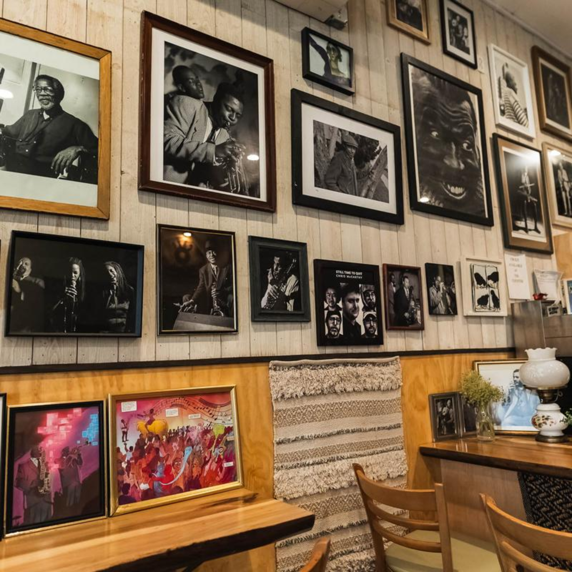 Café interior with wall of framed black-and-white jazz portraits above wooden tables and eclectic decor