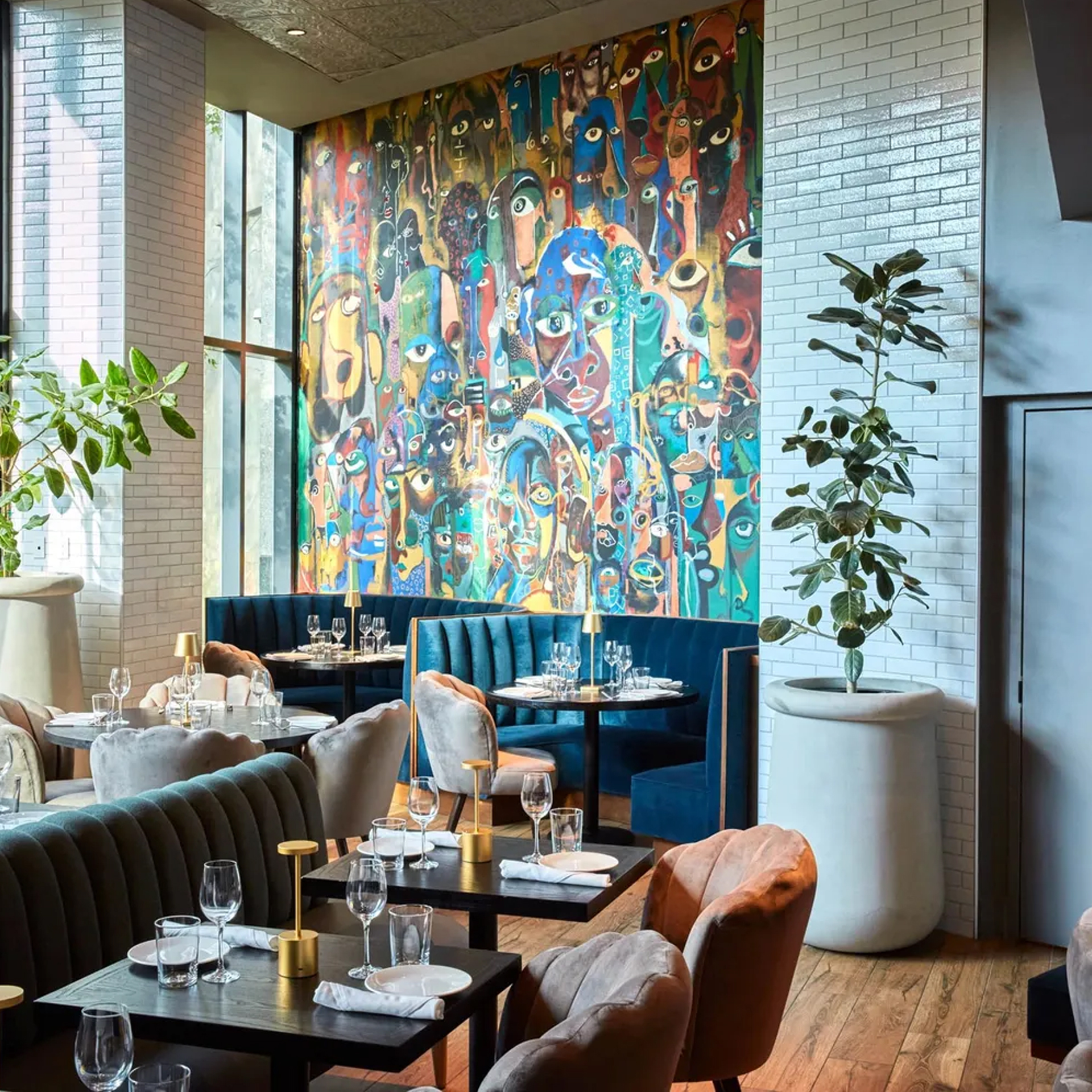 Modern restaurant interior with wooden floors, blue velvet seating, colorful mural, and natural light
