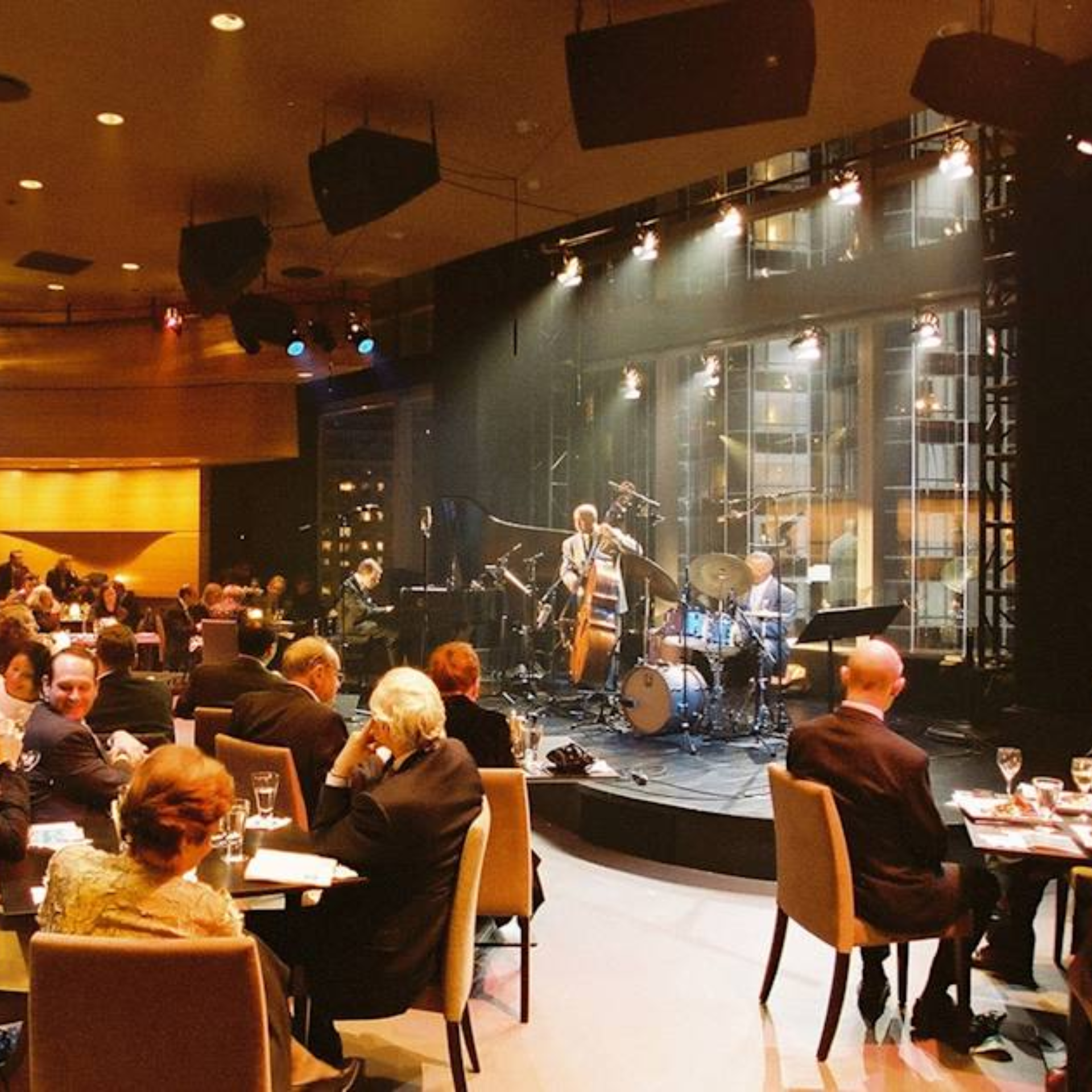 Live jazz band with piano, bass, and drums performing in elegant dinner setting with city view backdrop