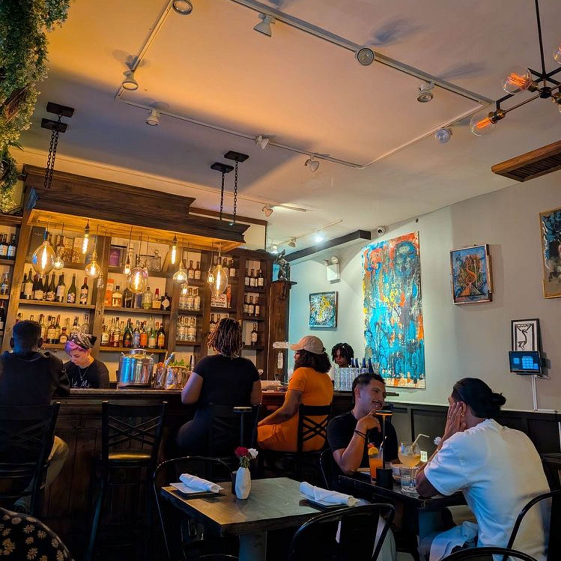 Cozy bar interior with wooden counter, bartender preparing drinks, shelves of liquor, and warm pendant lights