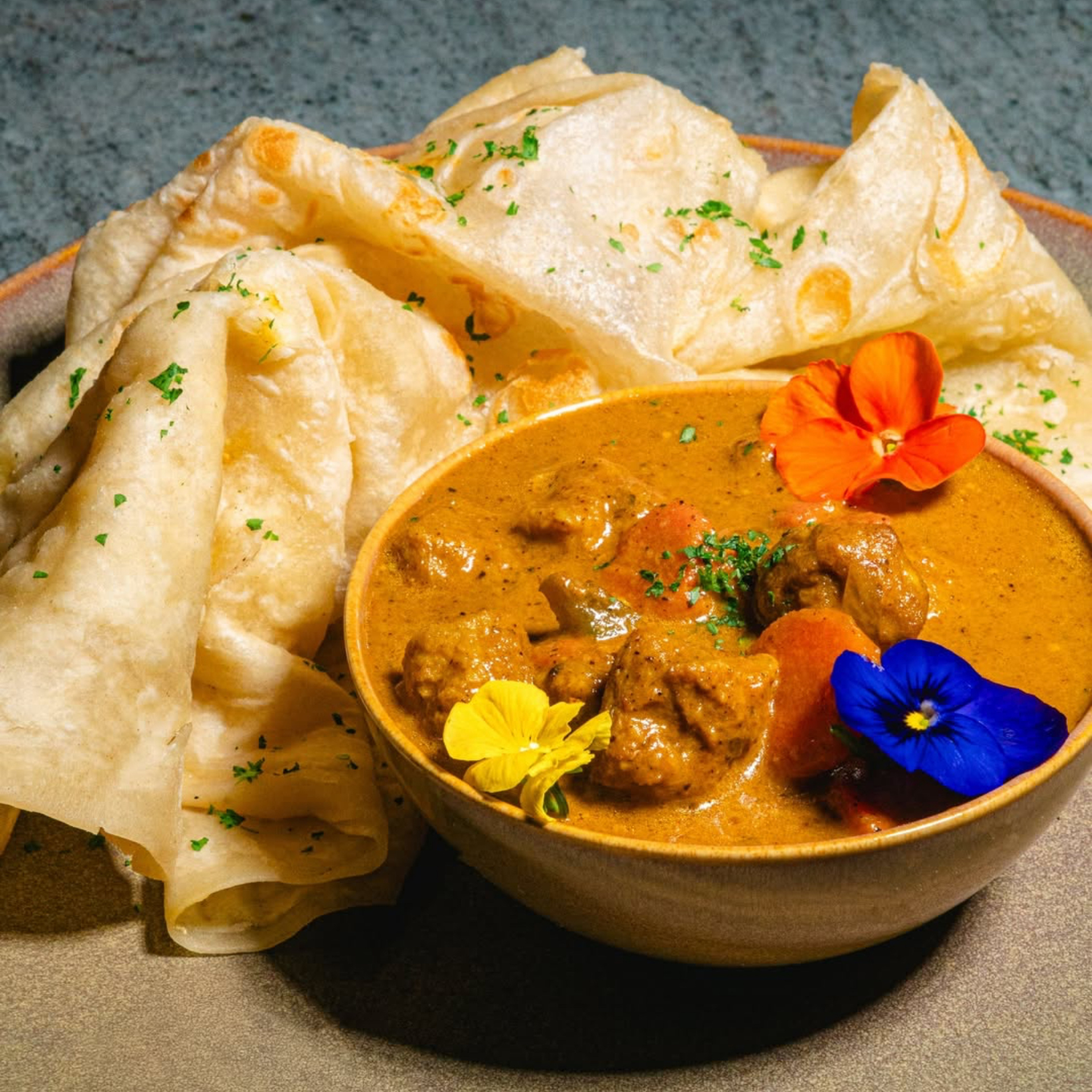 Plate with creamy curry garnished with edible flowers, served alongside folded flatbread
