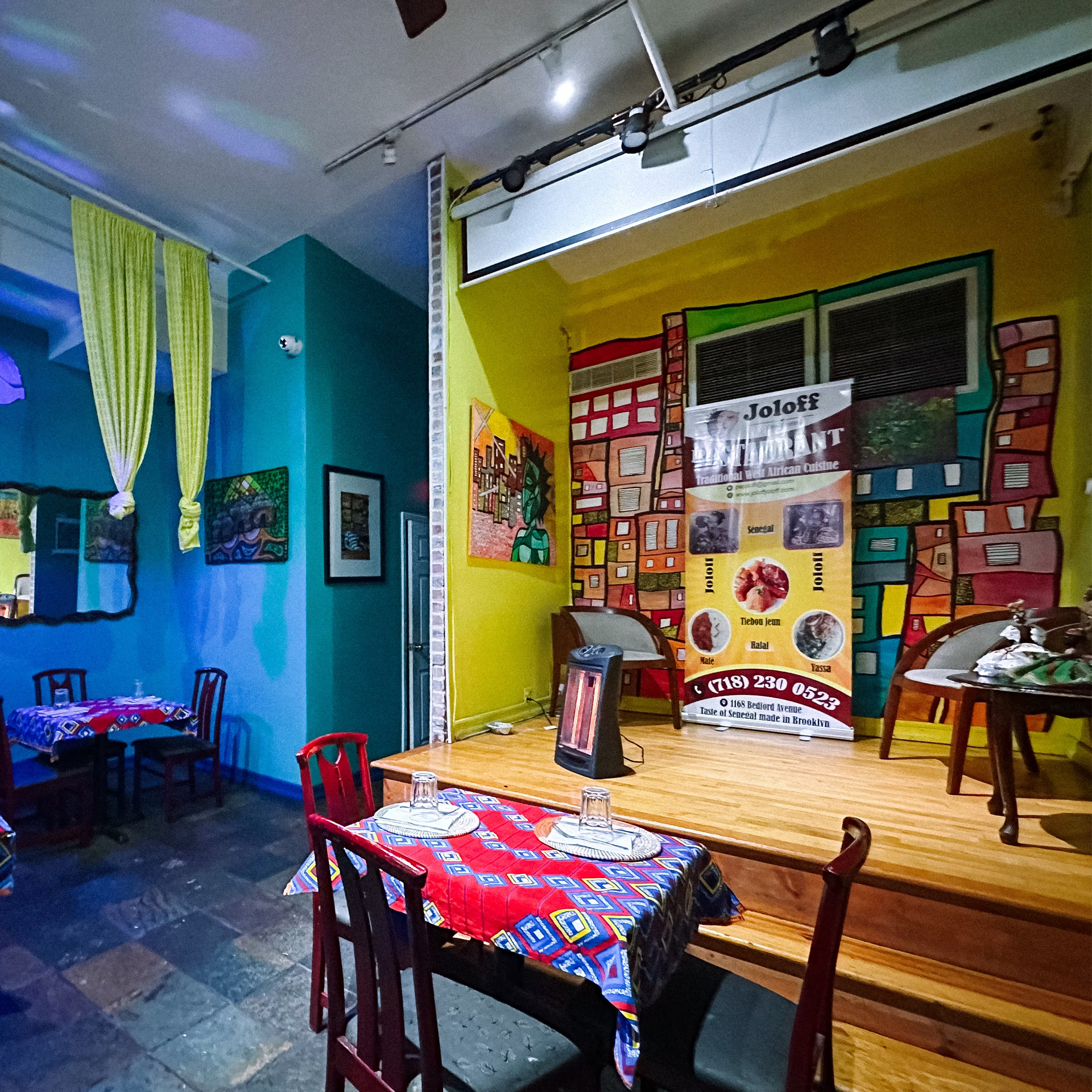 Colorful West African restaurant interior with vibrant tablecloths, artwork, and banner promoting Joloff cuisine