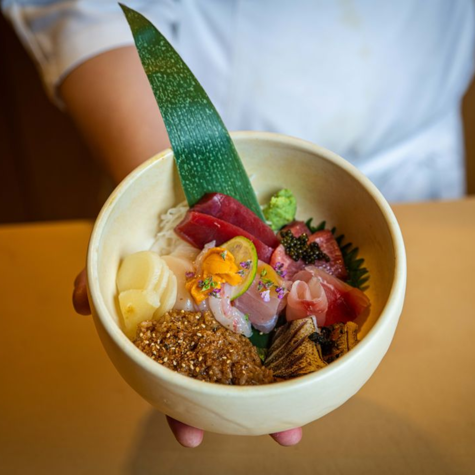 Assorted sashimi in a decorative bowl with garnishes, held by a chef