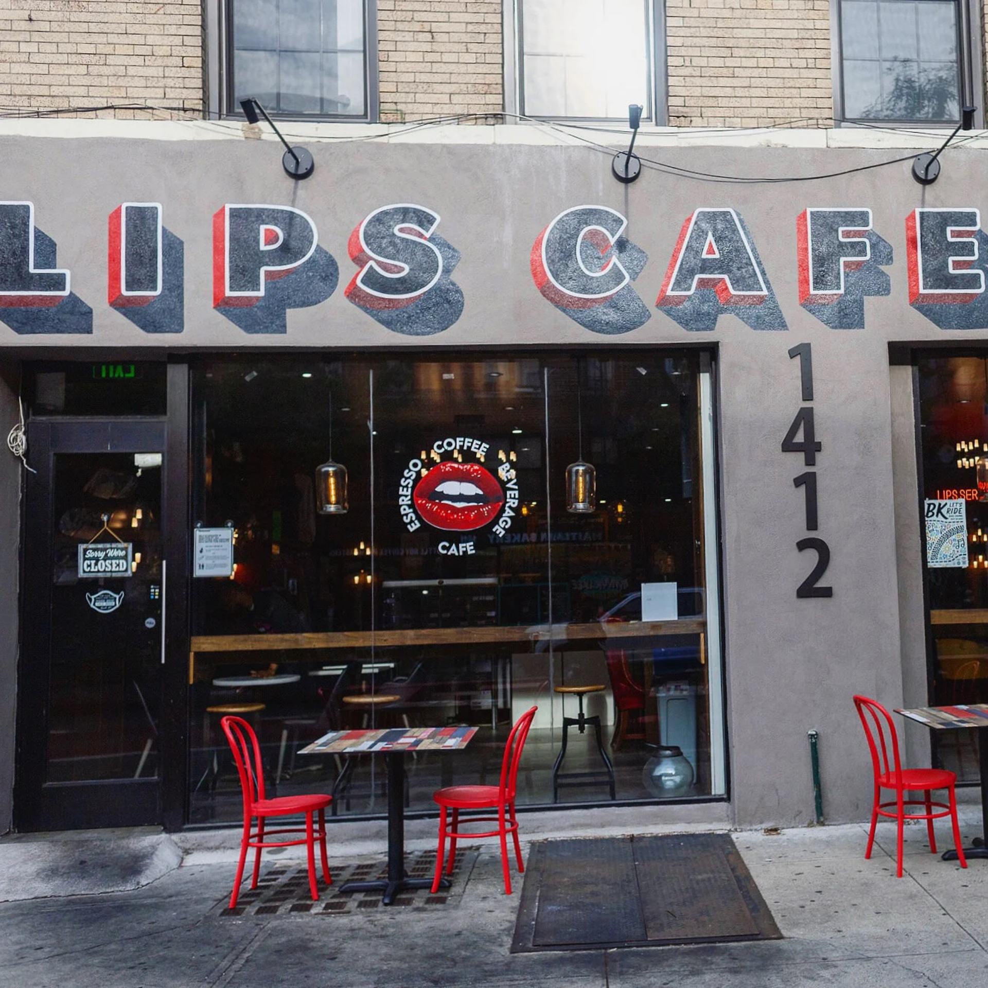 Exterior of Lips Café with bold signage, glass storefront, red chairs outside, and closed sign on door