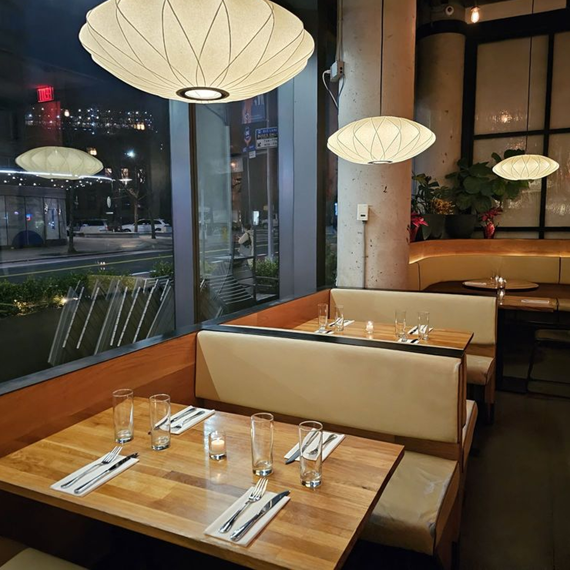 Modern restaurant interior at night with cushioned booth seating, warm pendant lights, and city view through large windows