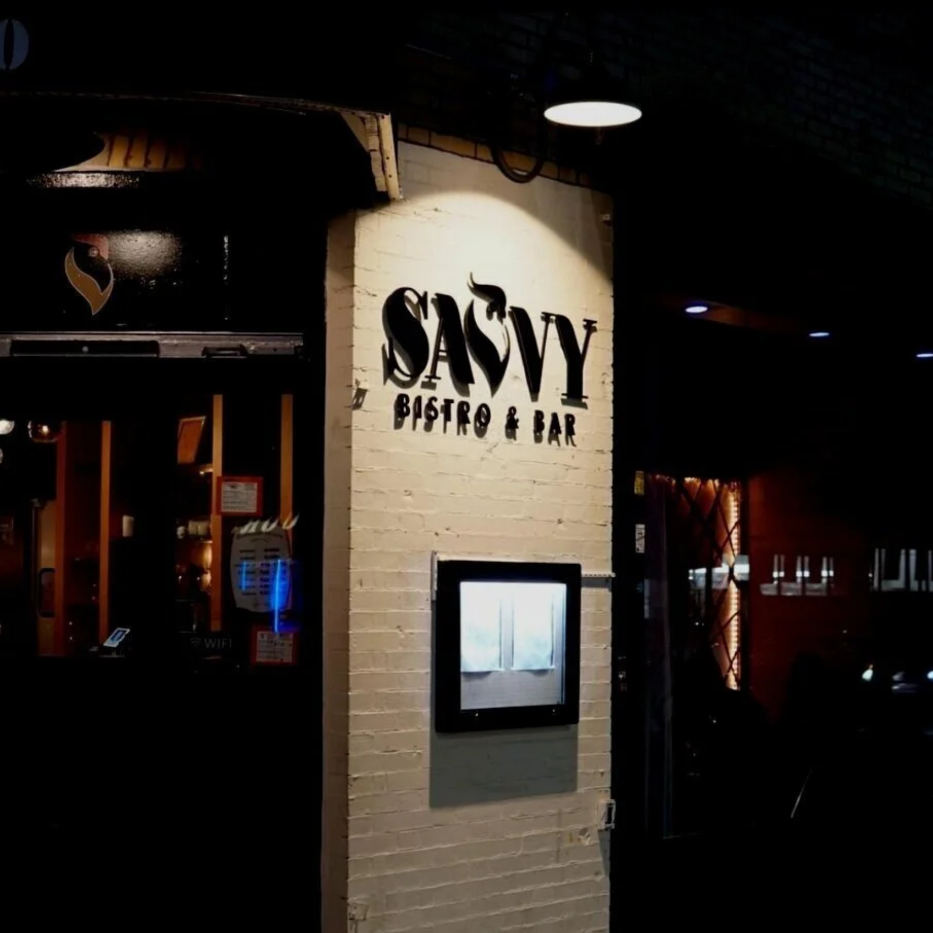 Exterior of Savvy Bistro & Bar with bold signage on brick wall and warmly lit entrance at night