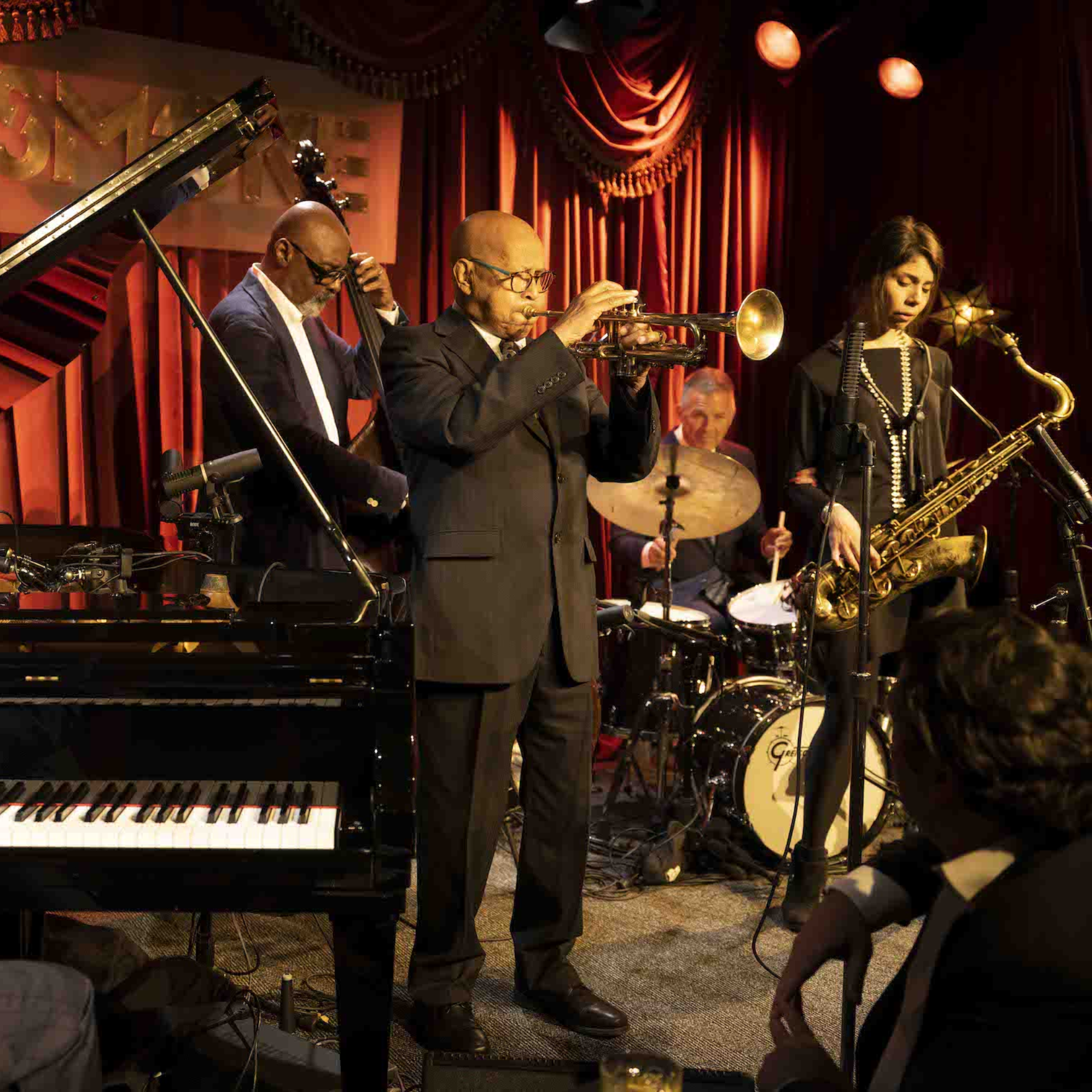 Jazz band with trumpet, saxophone, bass, drums, and piano performing on stage with red curtains