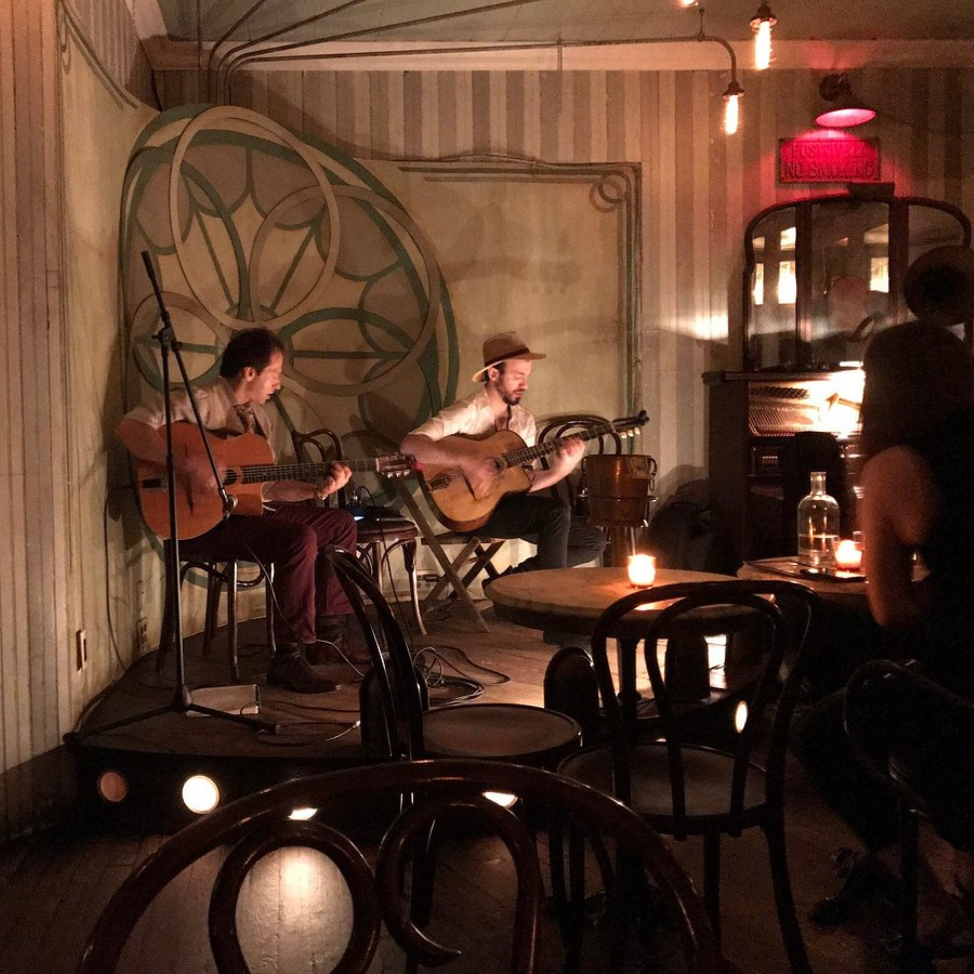 Brooklyn Jazz Clubs: Cozy café stage with two musicians playing acoustic guitars under warm candlelight and floral backdrop