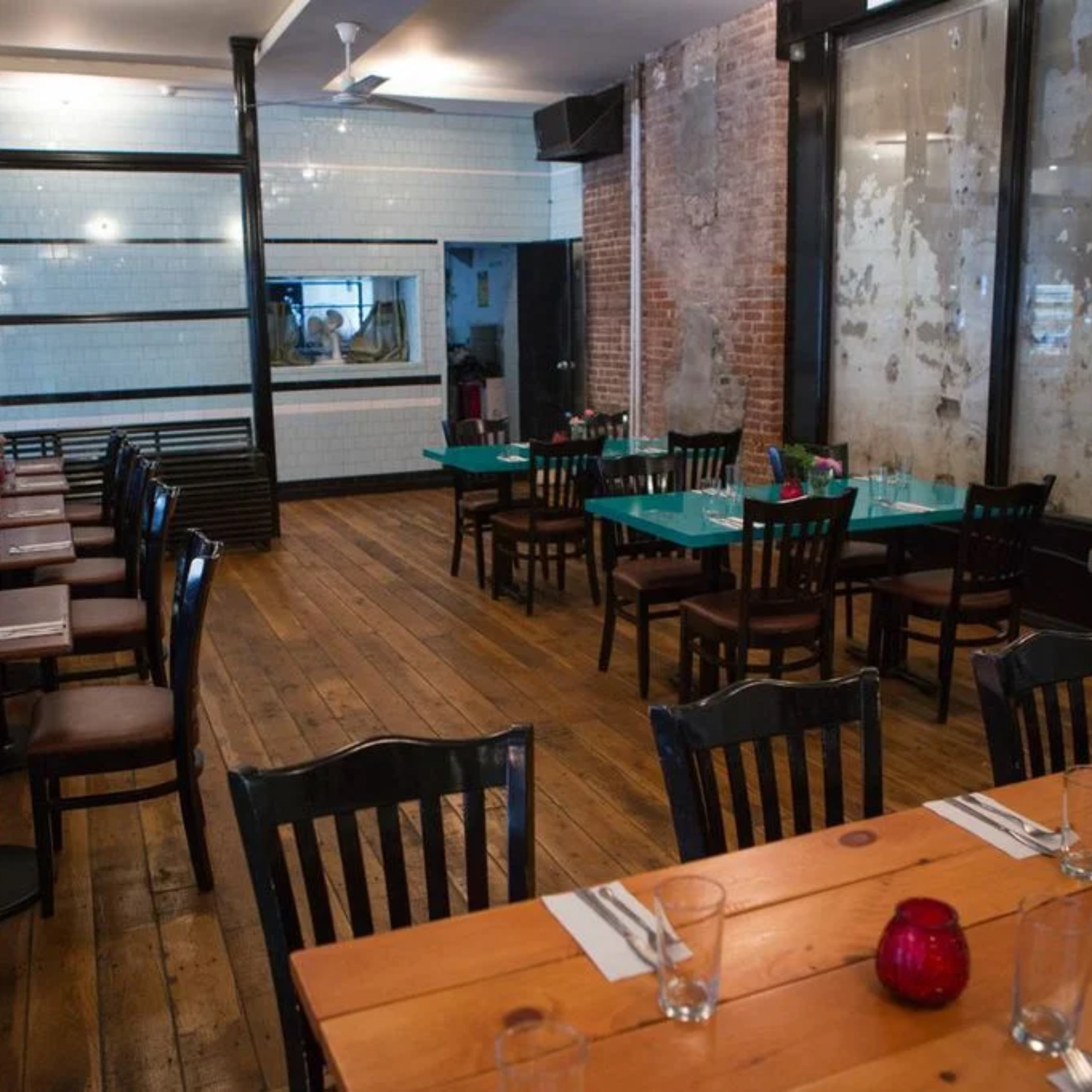 Restaurant interior with wooden floors, mixed rustic-modern design, turquoise and wood tables, and exposed brick walls
