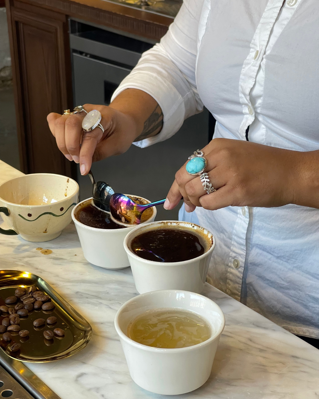 Person performing coffee cupping, tasting from small cups on a marble counter with beans and trays