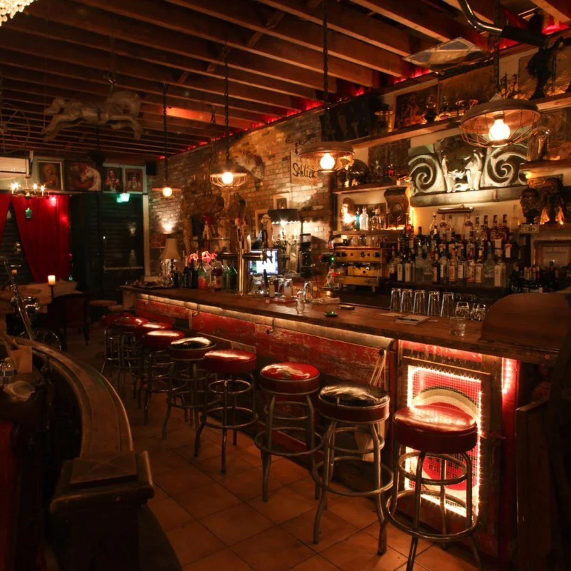 Rustic bar interior with wooden counter, red cushioned stools, exposed brick walls, and warm pendant lights