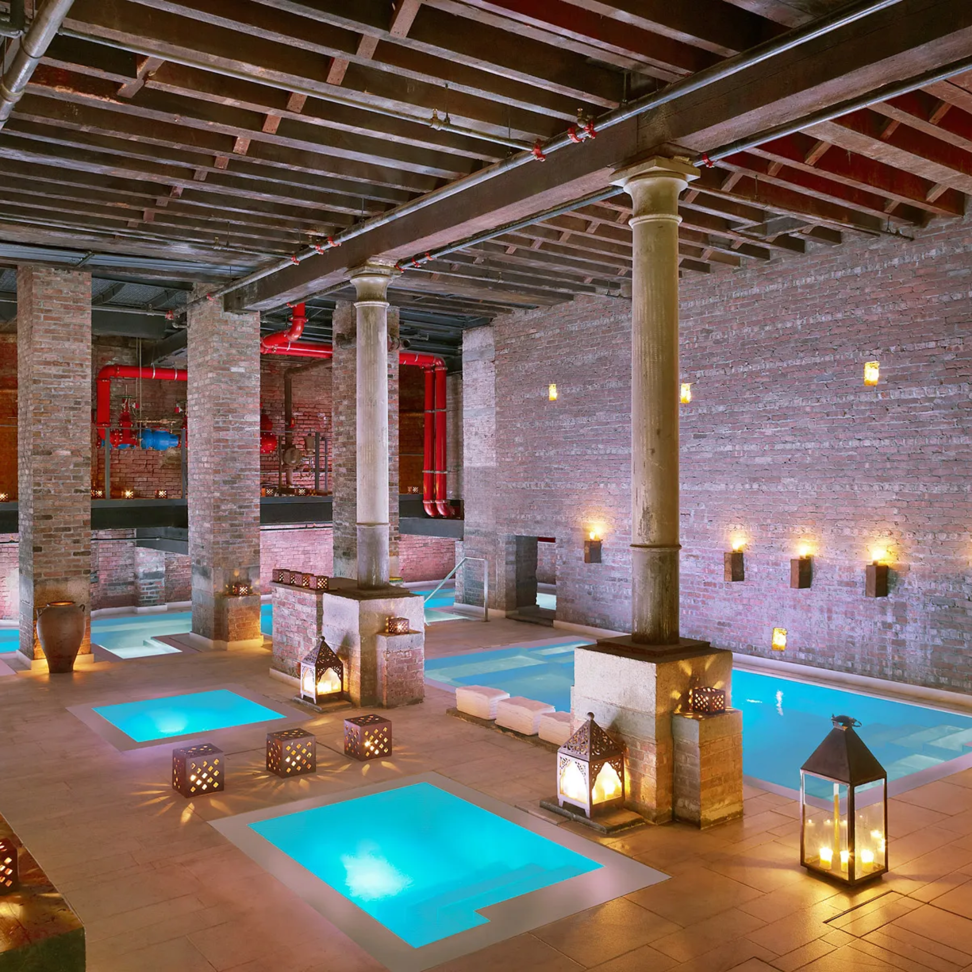 Indoor spa with glowing blue pools, brick walls, and candlelight
