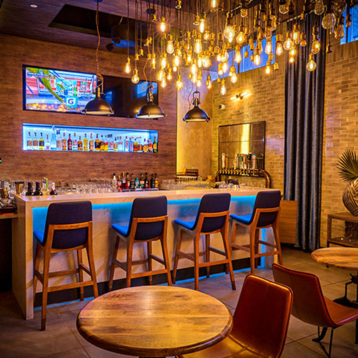 Modern bar with blue-lit counter, wooden stools, and hanging lights