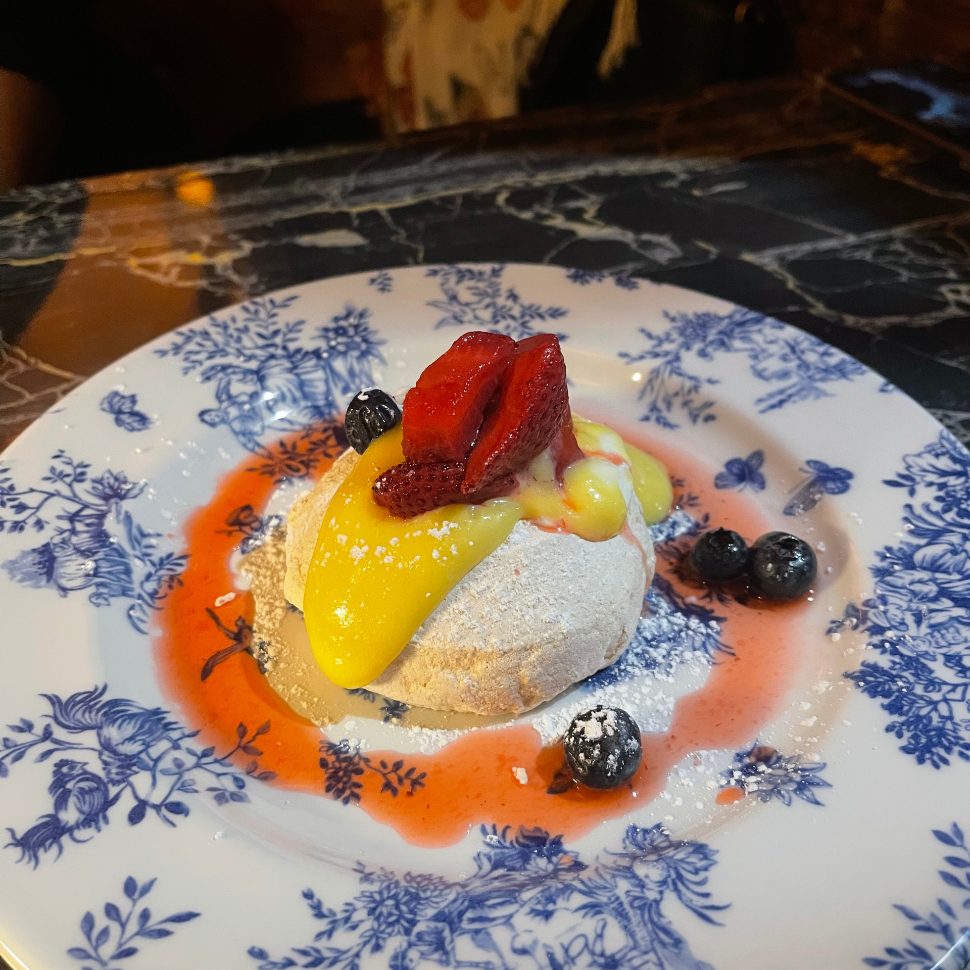 Plated dessert with meringue base, lemon curd, strawberries, blueberries, and berry sauce
