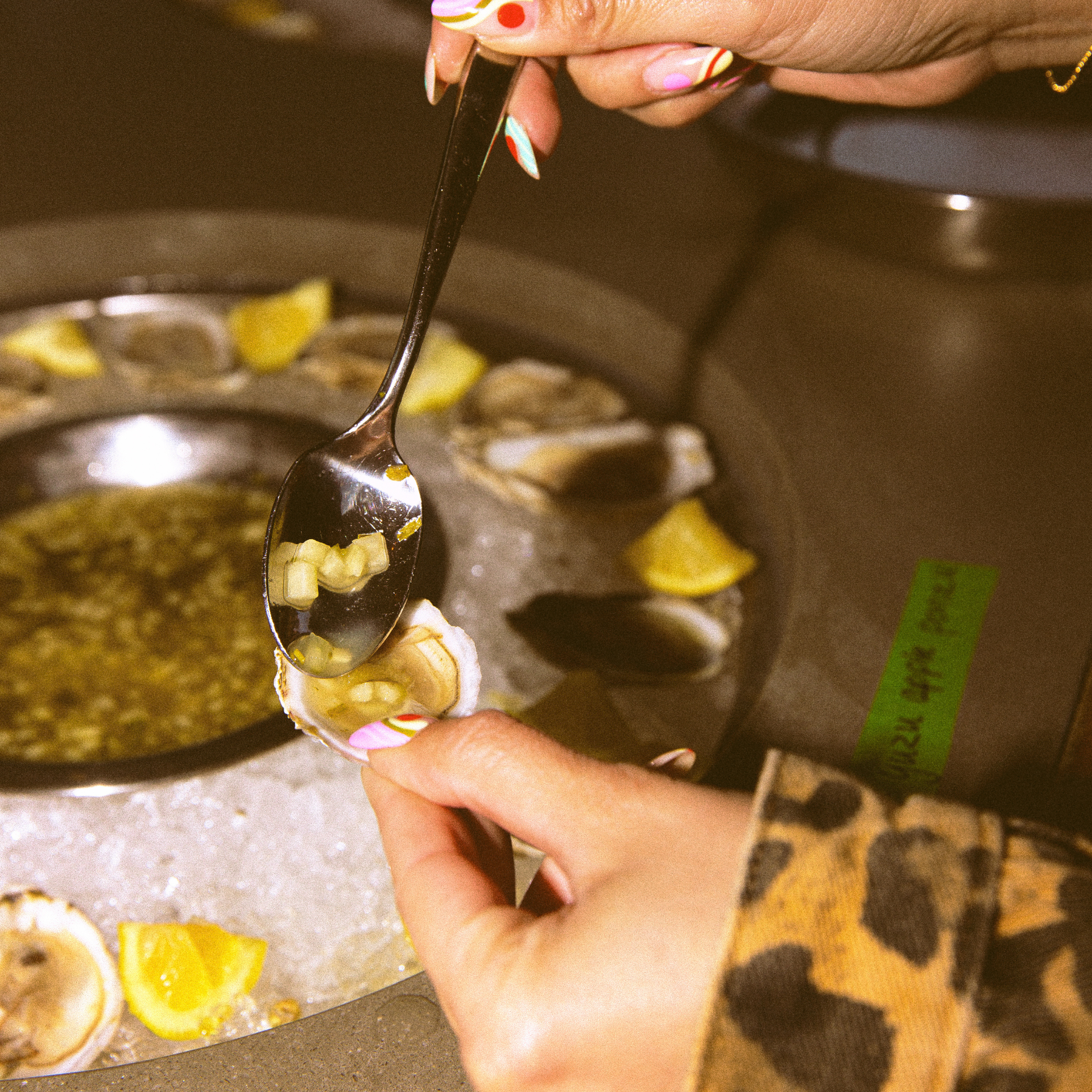 Person adding toppings to fresh oysters on ice, with lemon wedges nearby