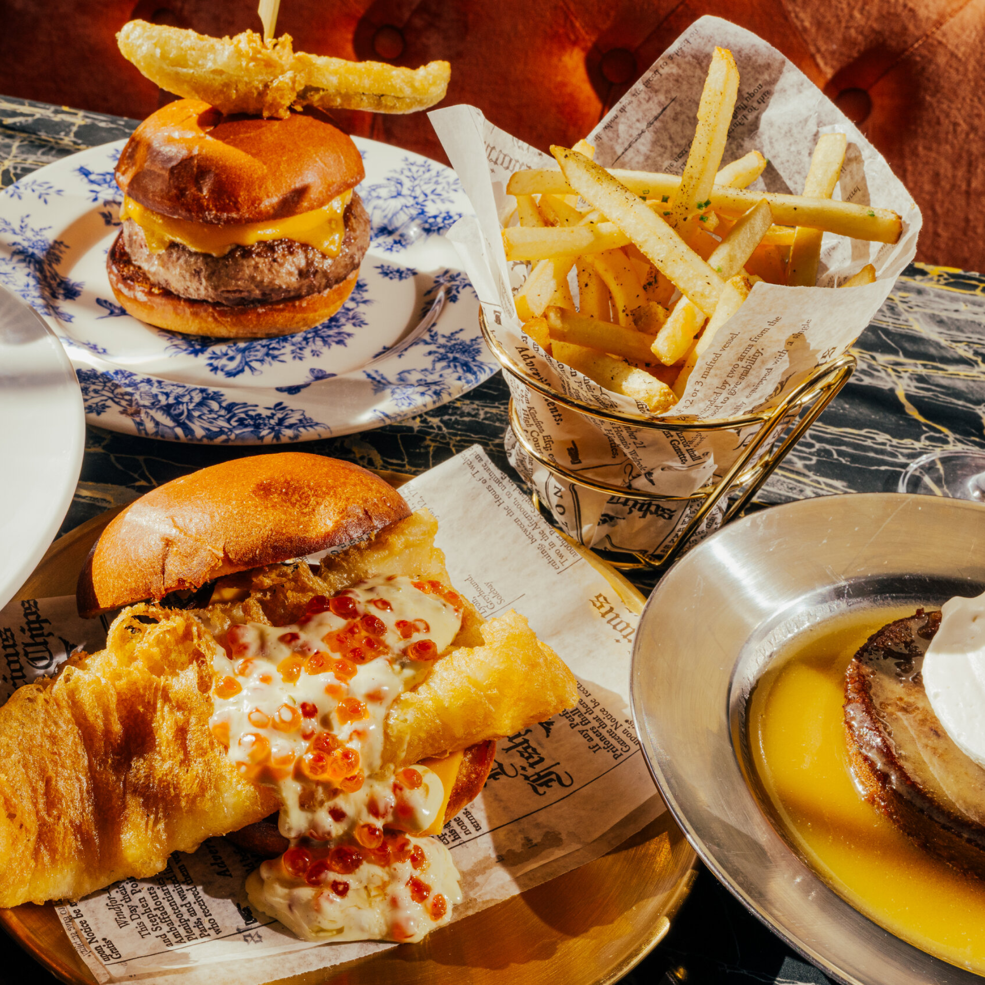 Table with gourmet burgers, fries in a metal cup, and a dessert with whipped cream on yellow sauce