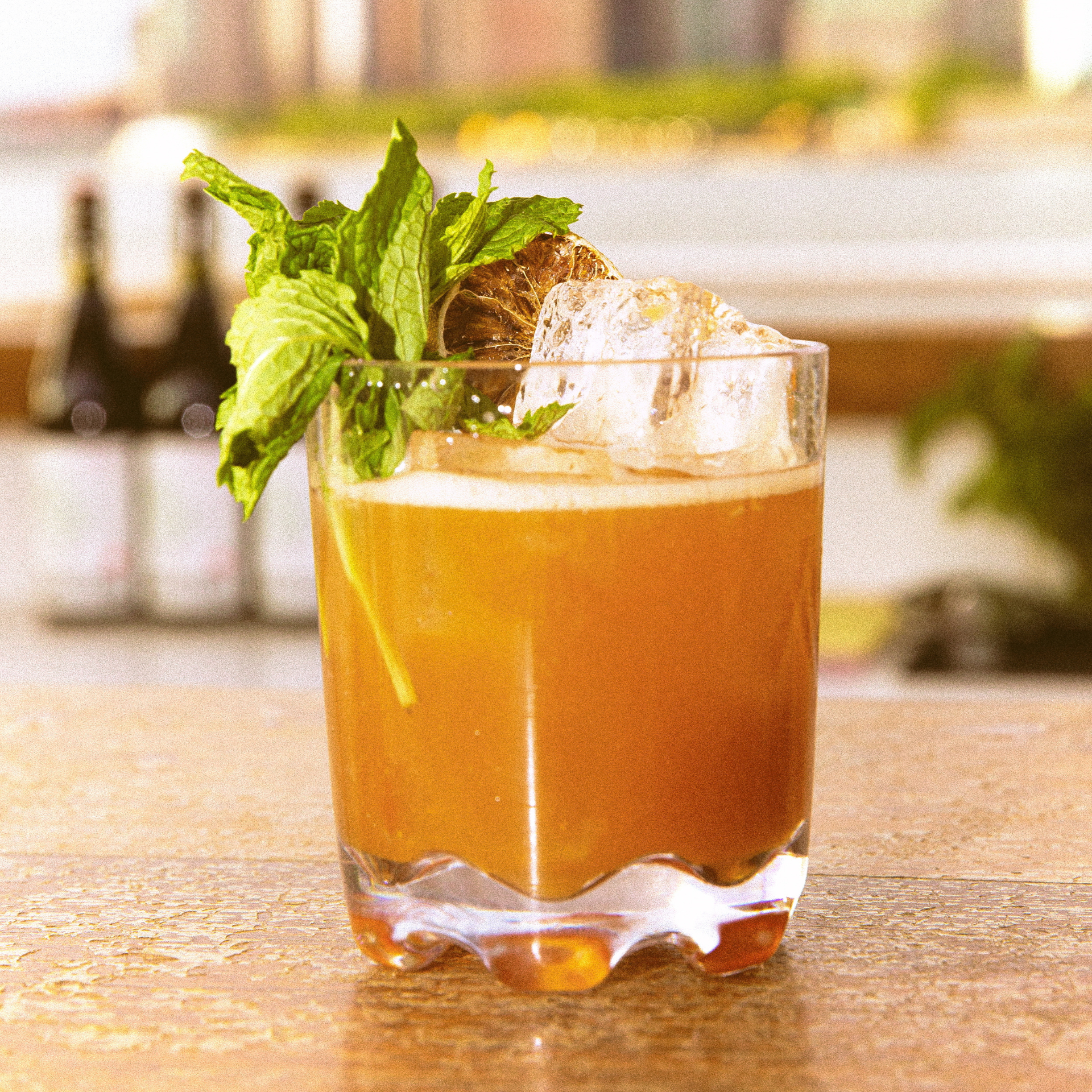 Six Coasts Governors Island: Amber cocktail in a short glass with ice, mint sprig, and dried citrus garnish on a bar counter