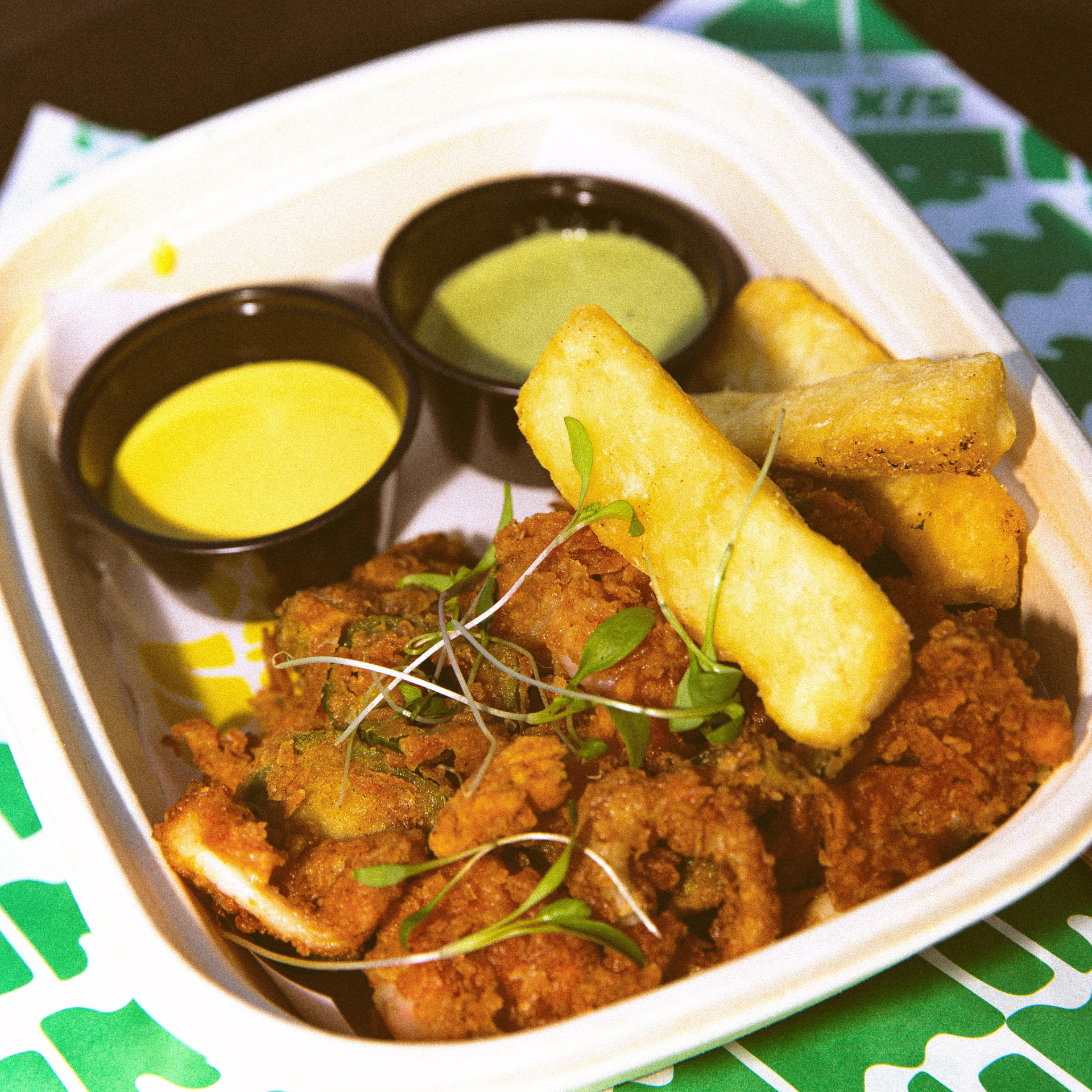 Fried seafood and yuca fries with microgreens, served in a container with yellow and green dipping sauces