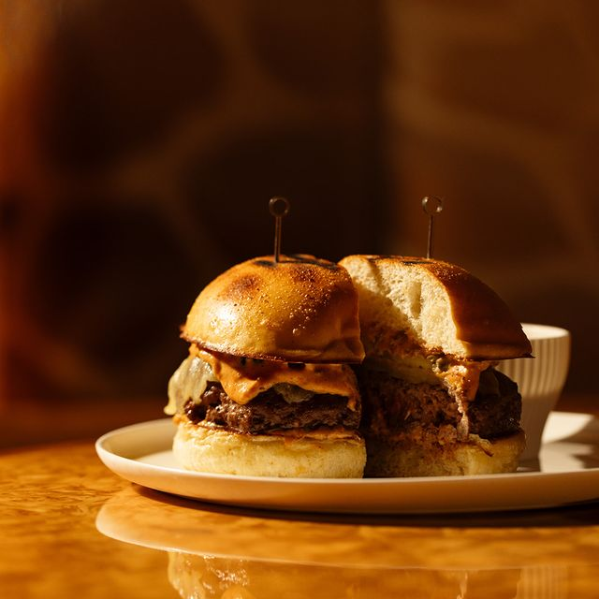 Close‑up of two NYC sliders with beef patties, melted cheese, and creamy sauce on white plate, cozy comfort food featured in daily things to do in NYC any day