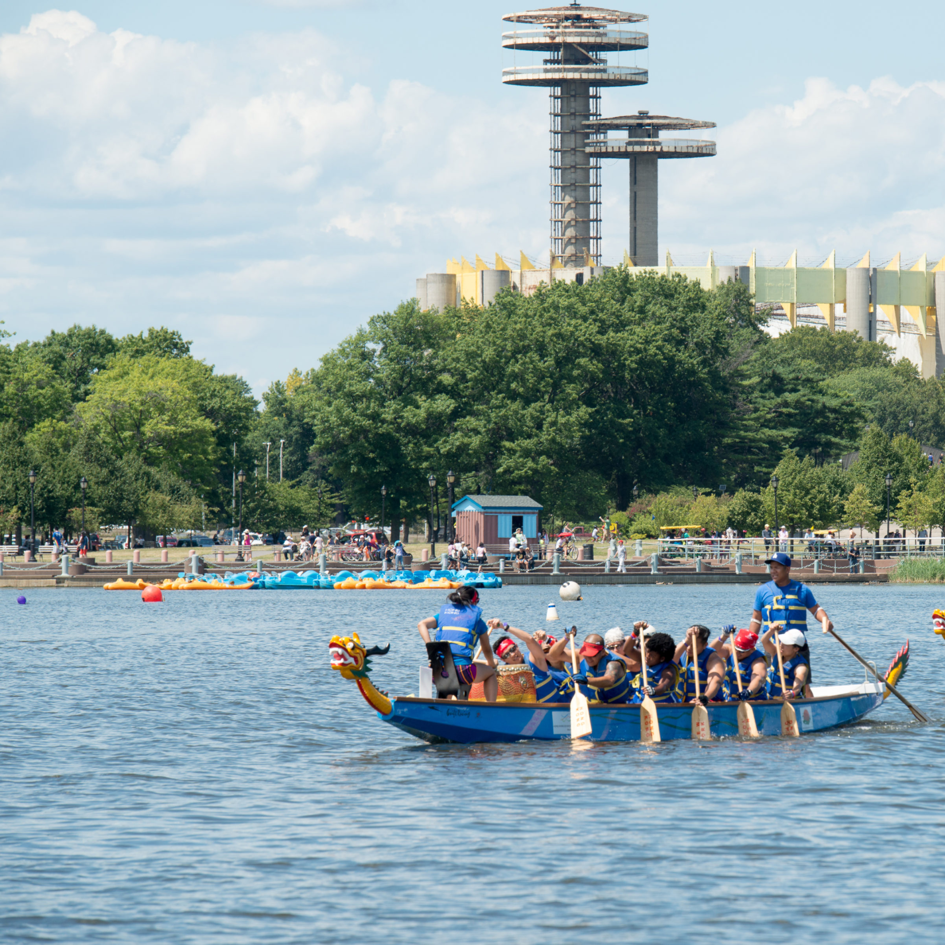Dragon boat with paddlers in life vests rowing on NYC waterfront with decorative dragon head and observation tower, cultural sport featured in daily things to do in NYC any day
