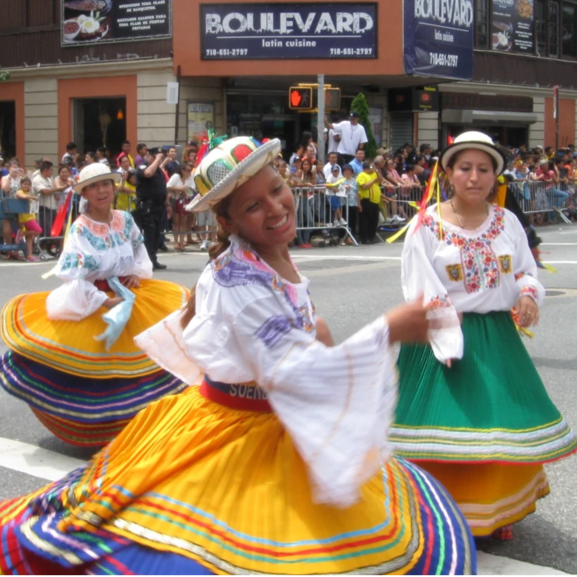 Three dancers in colorful folkloric skirts and embroidered blouses performing at NYC street parade with festive crowd, cultural heritage celebration featured in daily things to do in NYC any day