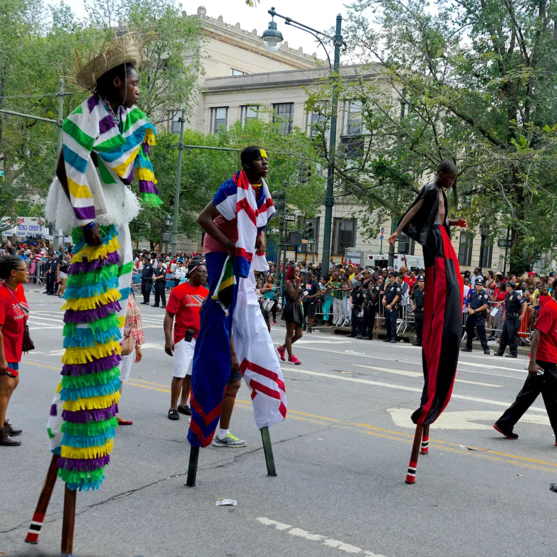 Three stilt walkers in colorful costumes perform in a city parade