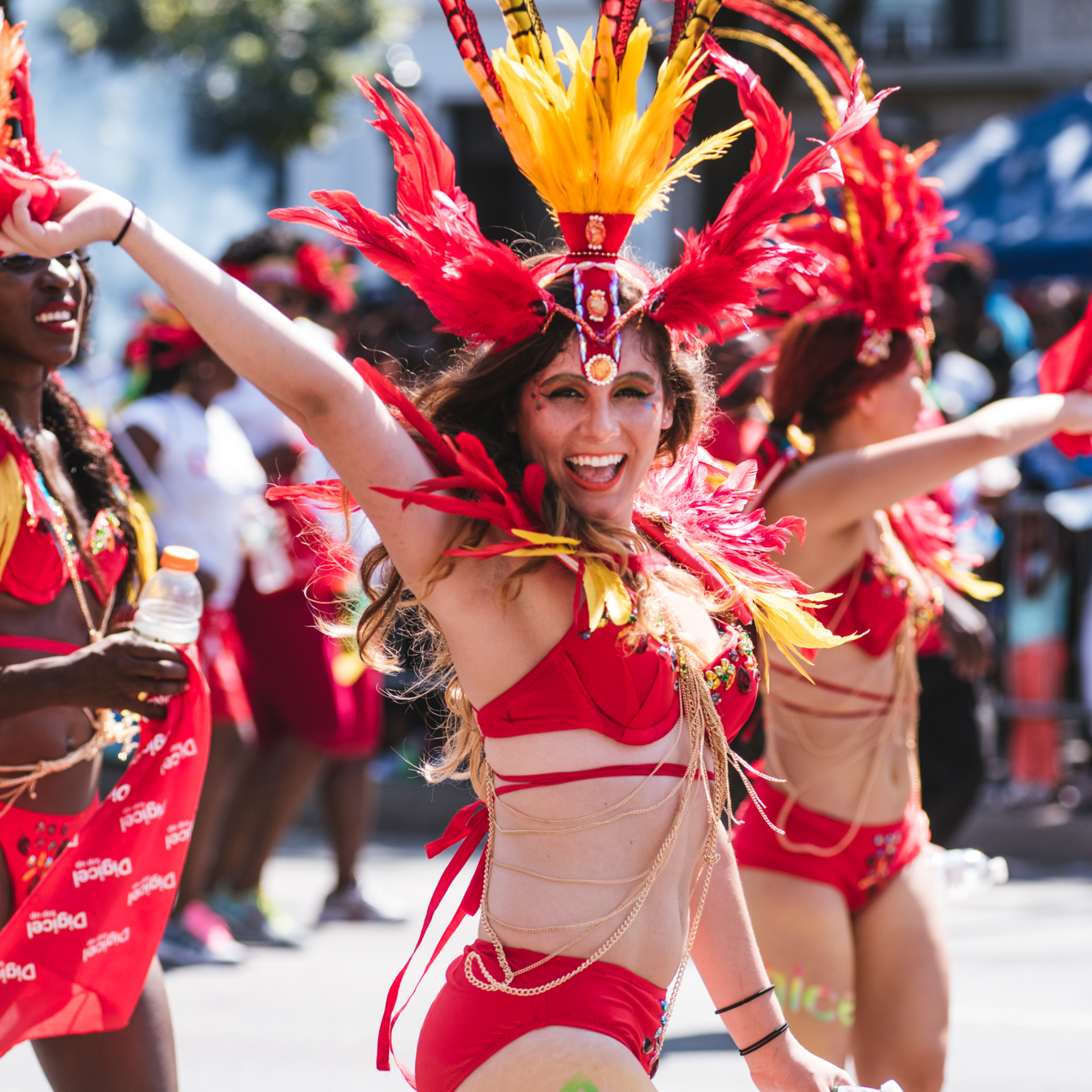 Performer in red and yellow feathered costume dancing at NYC carnival parade with festive crowd, cultural street celebration featured in daily things to do in NYC any day