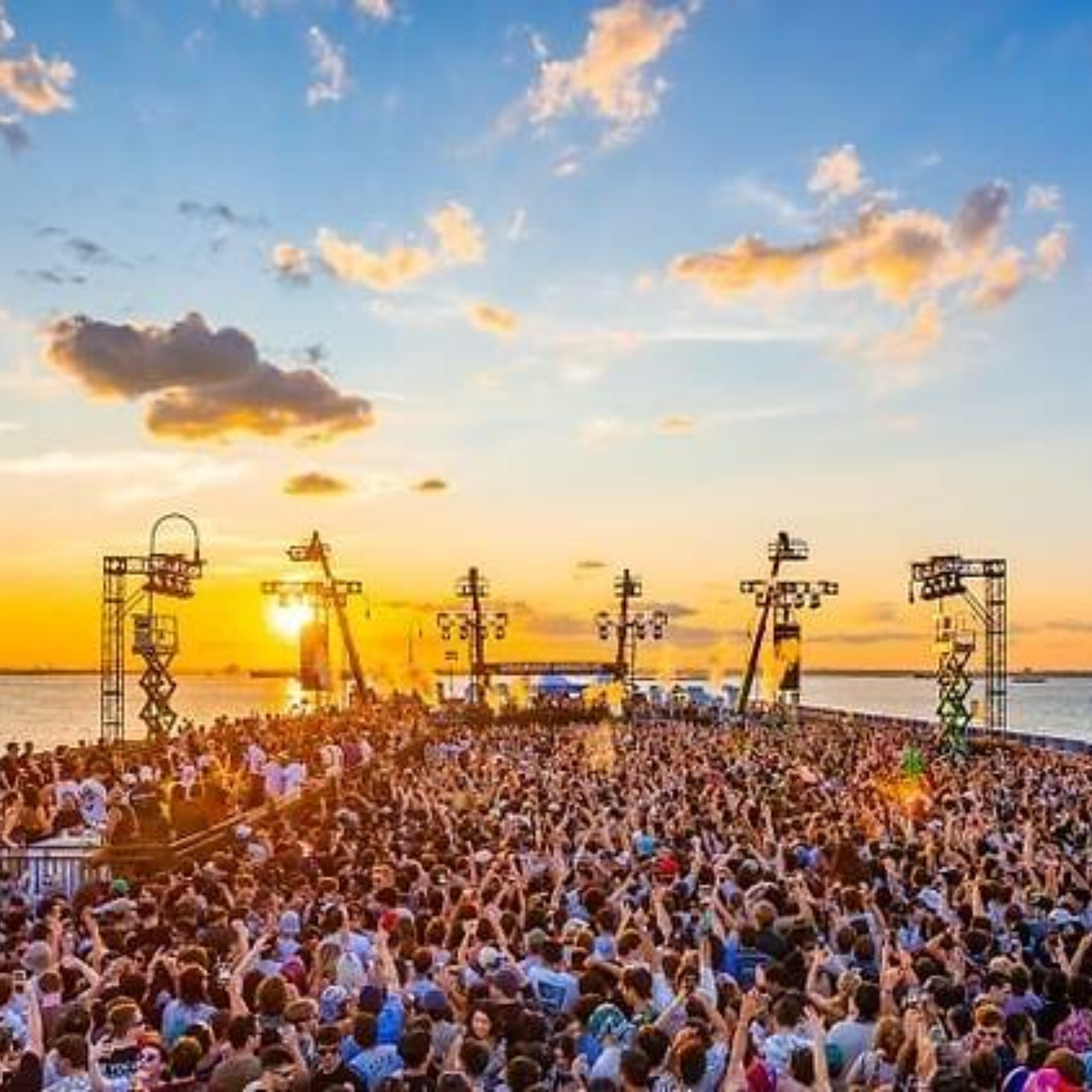NYC waterfront music festival at sunset with massive crowd raising hands before stage, golden glow over water featured in daily things to do in NYC any day