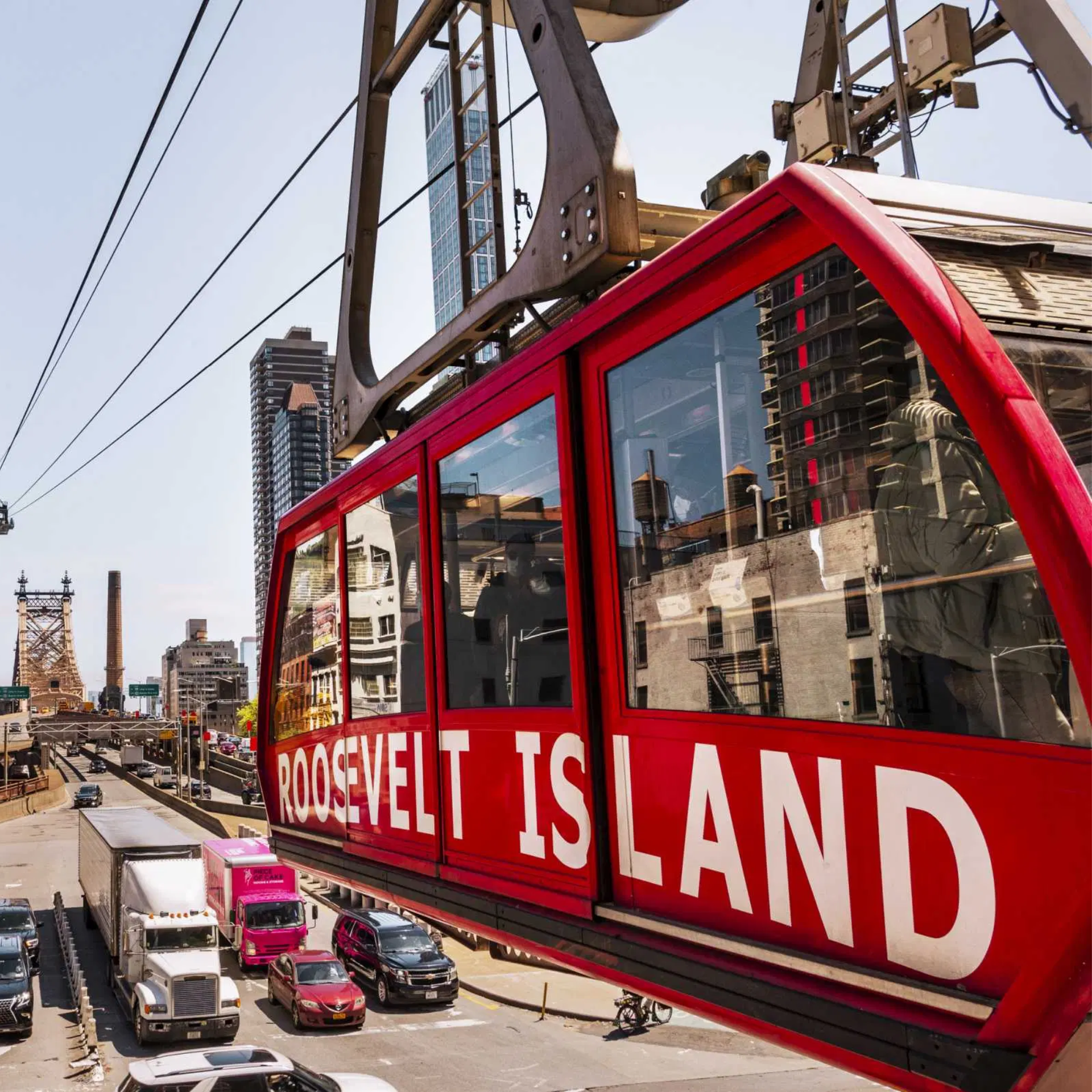 Roosevelt Island Tramway red cable car suspended above New York City street with Queensboro Bridge and tall buildings in background