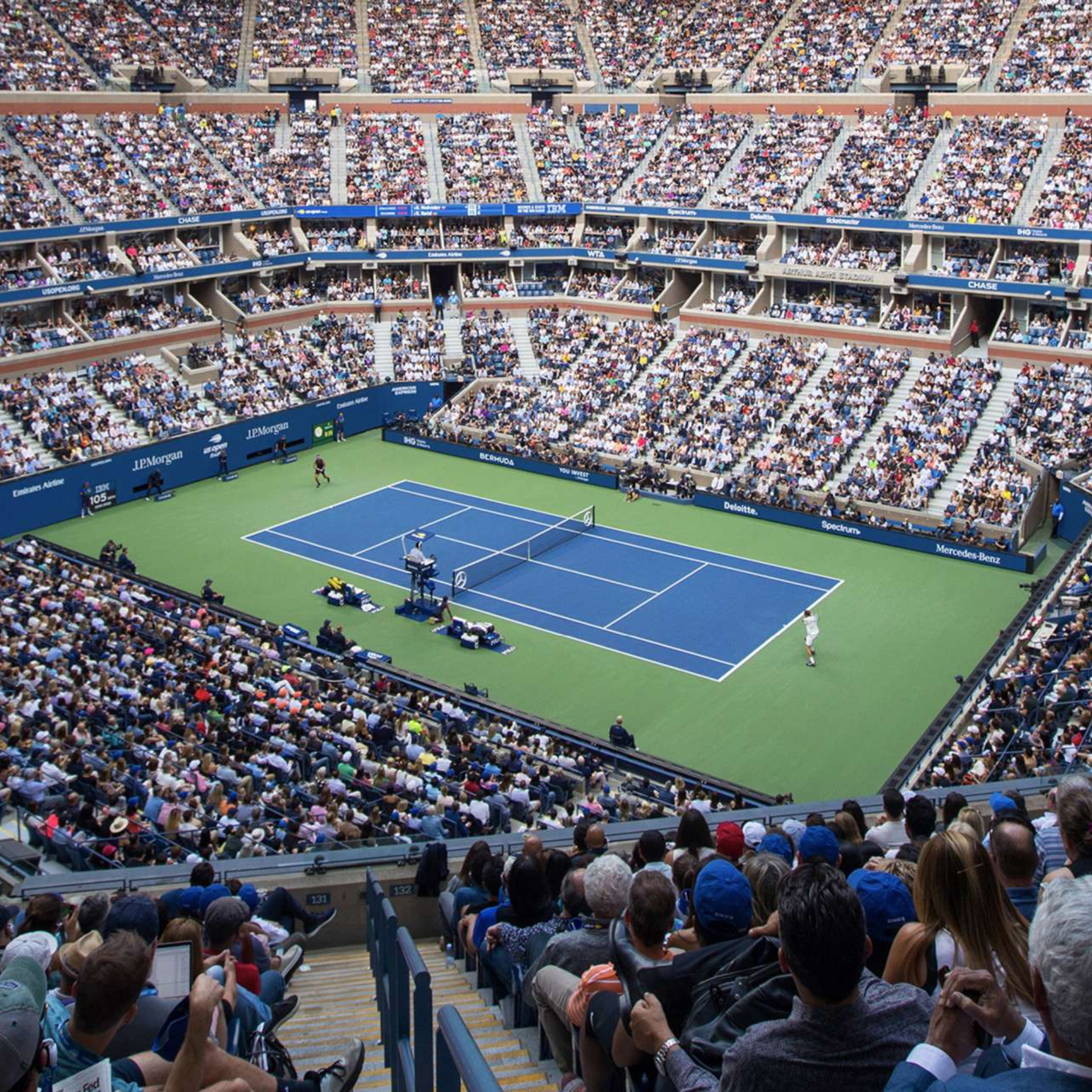 NYC tennis stadium packed with spectators watching professional match on blue court, major sports event featured in daily things to do in NYC any day