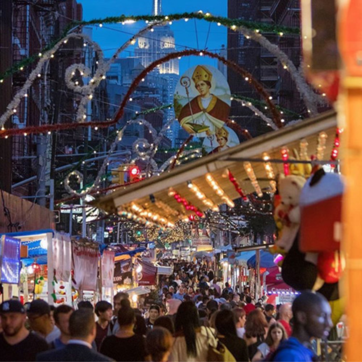 NYC Labor Day street festival with vendor stalls, decorative arches, saint image, and Empire State Building lit in background, lively evening celebration featured in daily things to do in NYC any day
