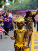 Child in gold costume with sun‑shaped headpiece holding American flag at NYC Labor Day parade, community celebration featured in daily things to do in NYC any day