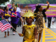 Child in gold costume with sun‑shaped headpiece holding American flag at NYC Labor Day parade, community celebration featured in daily things to do in NYC any day