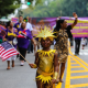 Child in gold costume with sun‑shaped headpiece holding American flag at NYC Labor Day parade, community celebration featured in daily things to do in NYC any day