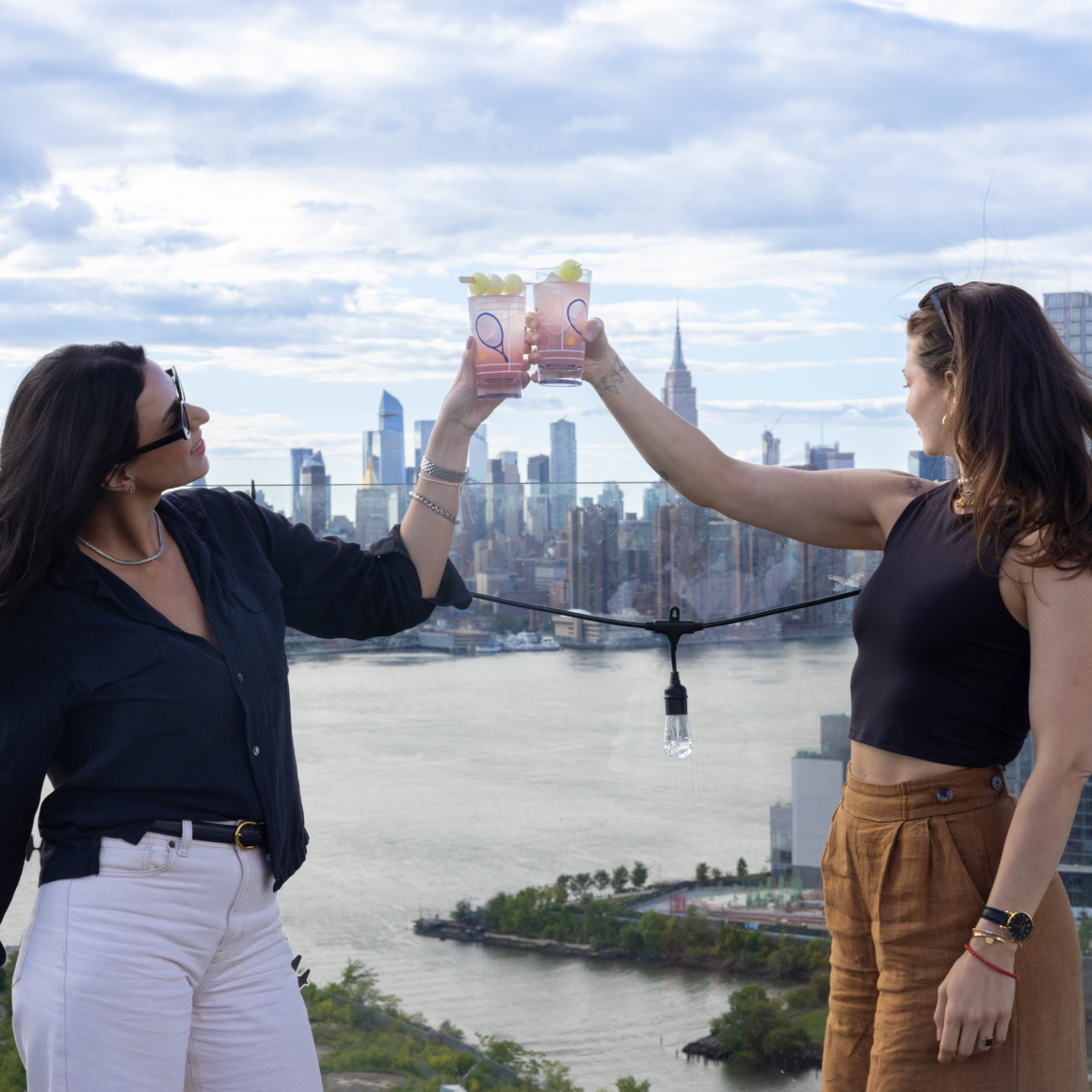 Two people toasting pink drinks on NYC rooftop terrace