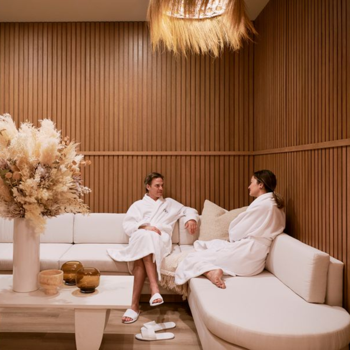 Two people in white robes on sofa in wood‑paneled spa room