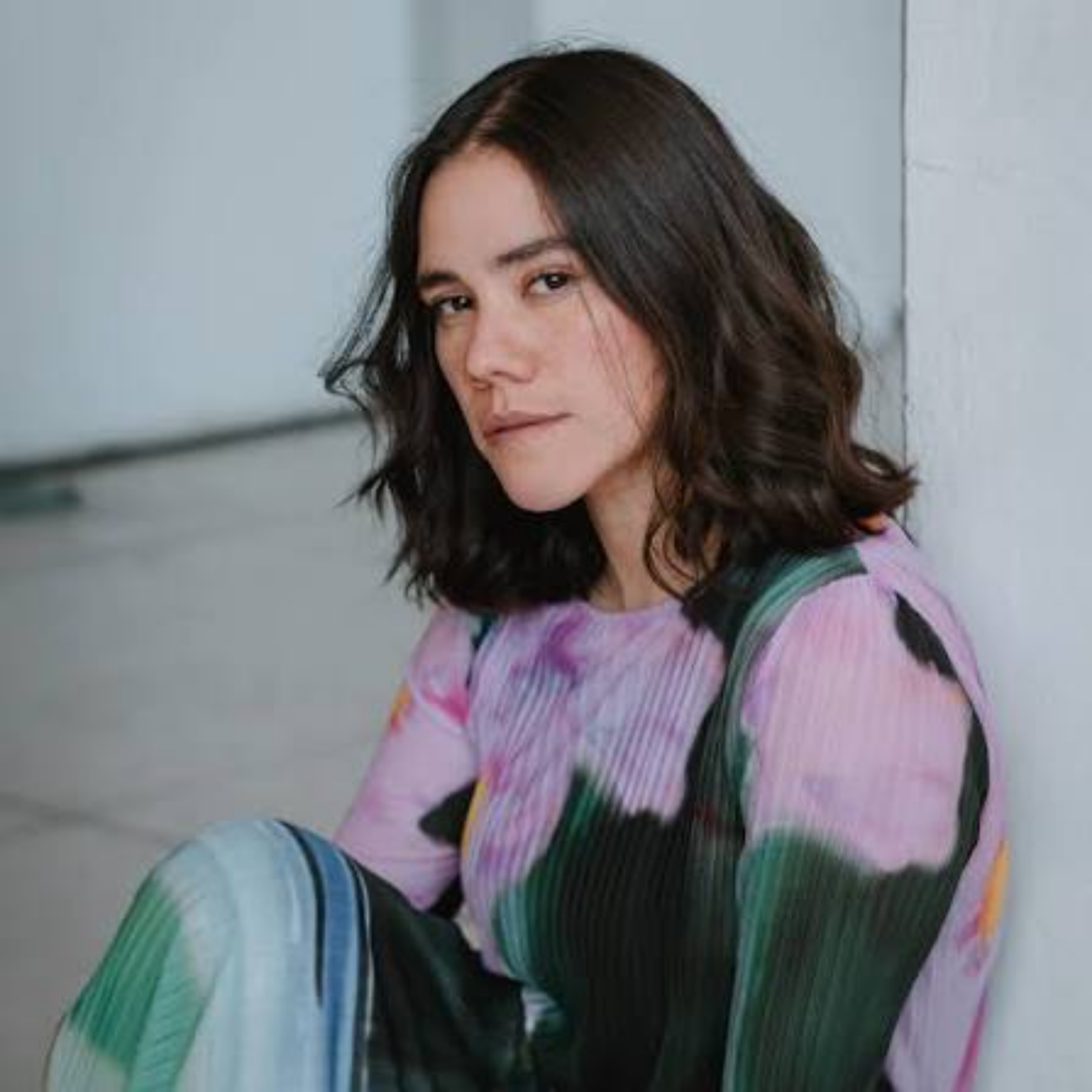 Person in colorful abstract pleated top seated indoors against white wall at NYC Labor Day fashion portrait session, artistic style featured in daily things to do in NYC any day